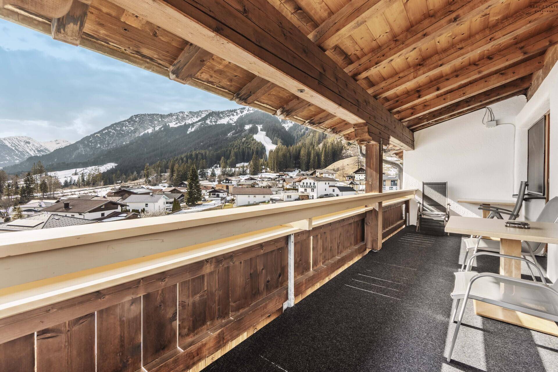 Geräumiger Balkon mit Holzbalken, Sitzgelegenheiten und Panoramablick auf die verschneiten Berge.