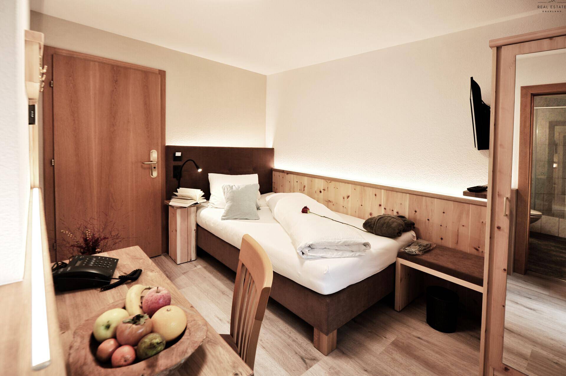 Schlafzimmer mit Einzelbett, Holzakzenten und einem Schreibtischbereich mit Obstschale.