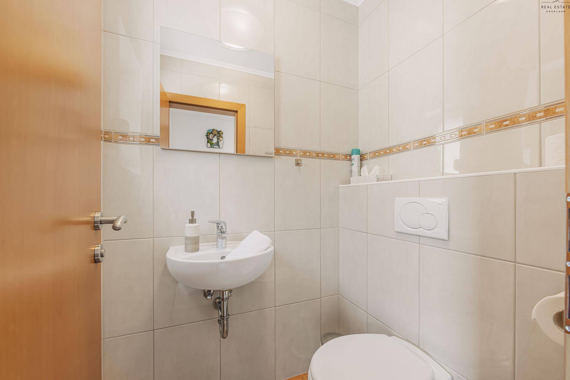 Kleines Gäste-WC mit Waschbecken und hellen Fliesen an den Wänden.