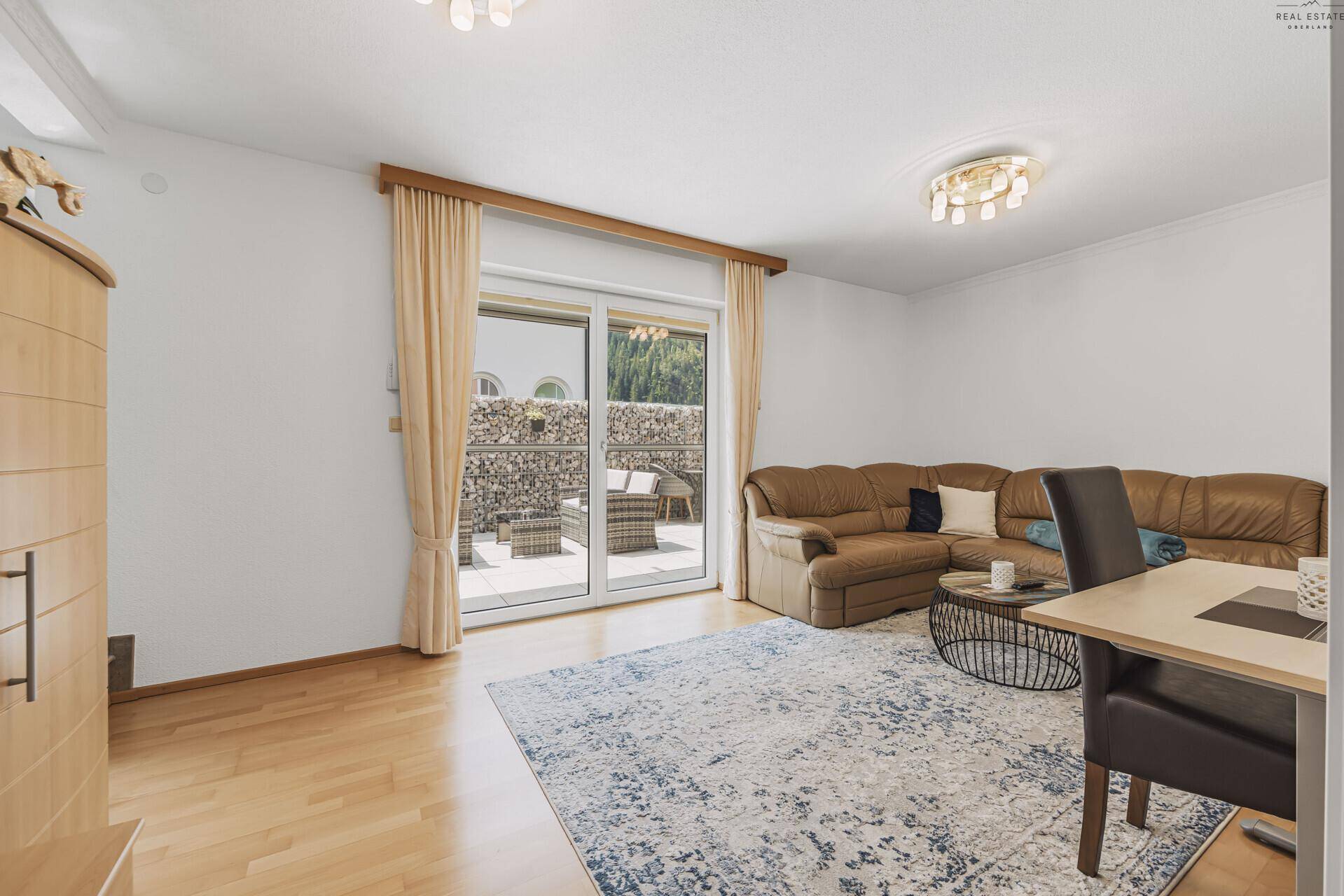 Helles Wohnzimmer mit bequemer Couch, Holzboden und direktem Zugang zur Terrasse.