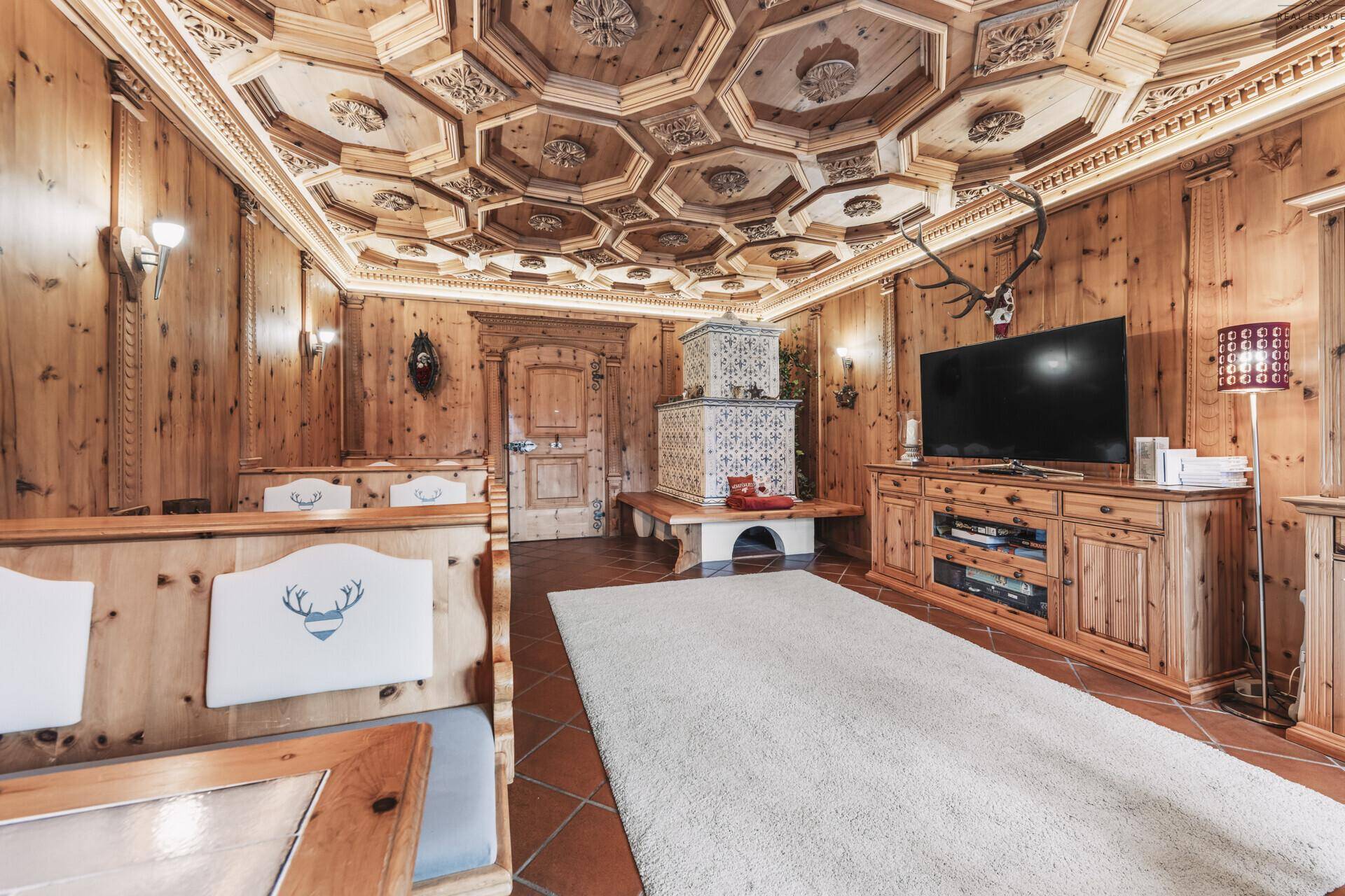 Rustikales Wohnzimmer im alpinen Stil mit Holzeinrichtung, Kachelofen und geschnitzter Decke.
