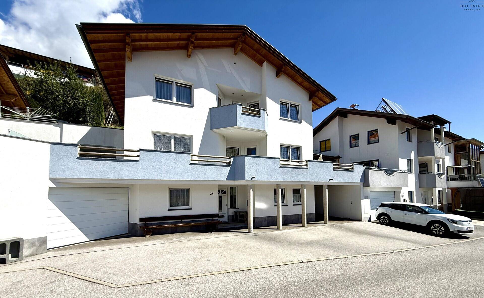 Geräumiges weißes Wohnhaus mit blauen Balkonen, Carport und gepflegter Auffahrt.