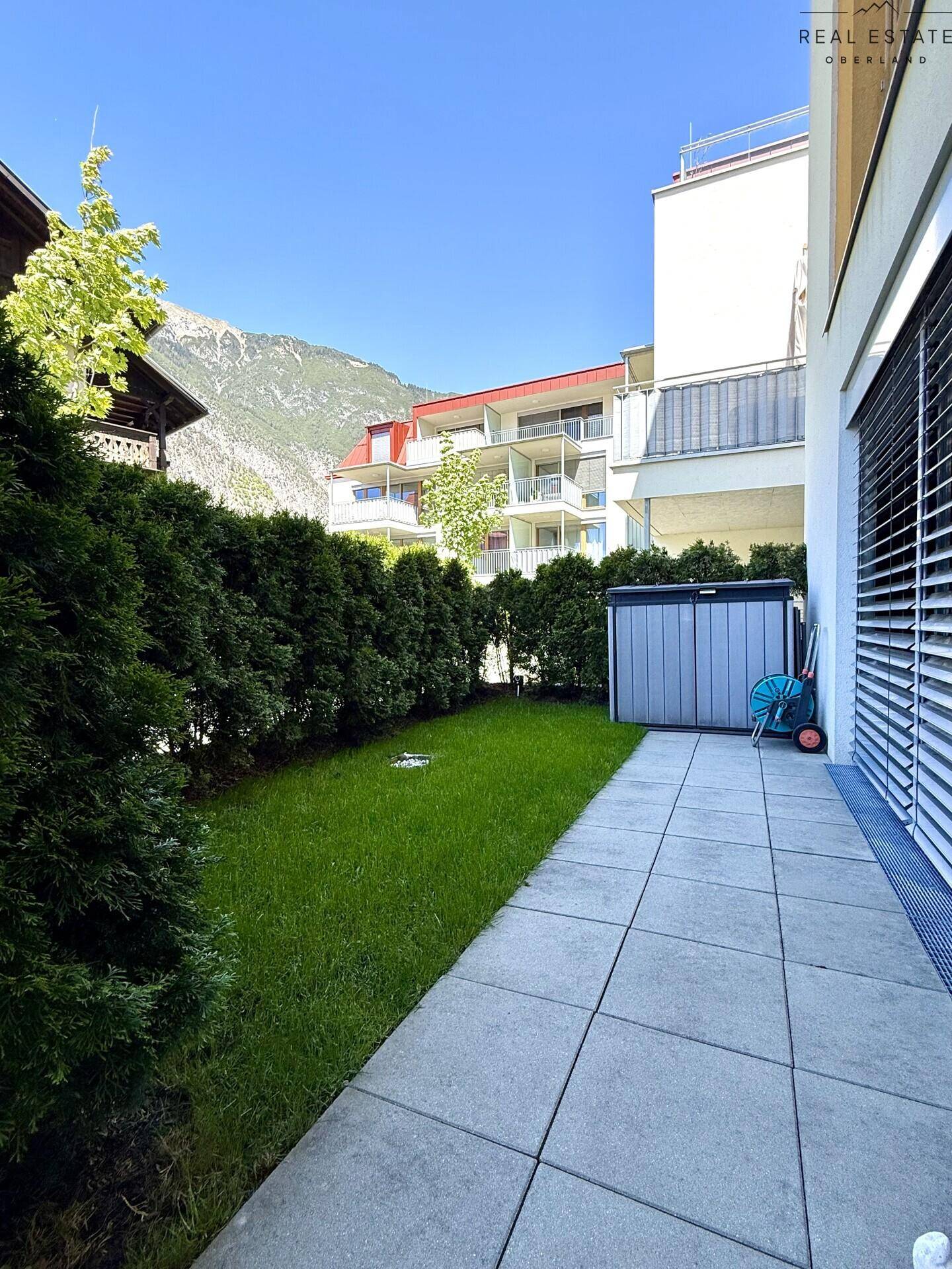 Kleiner, gepflegter Gartenbereich mit Terrasse, hohen Hecken und praktischem Gartenschuppen.