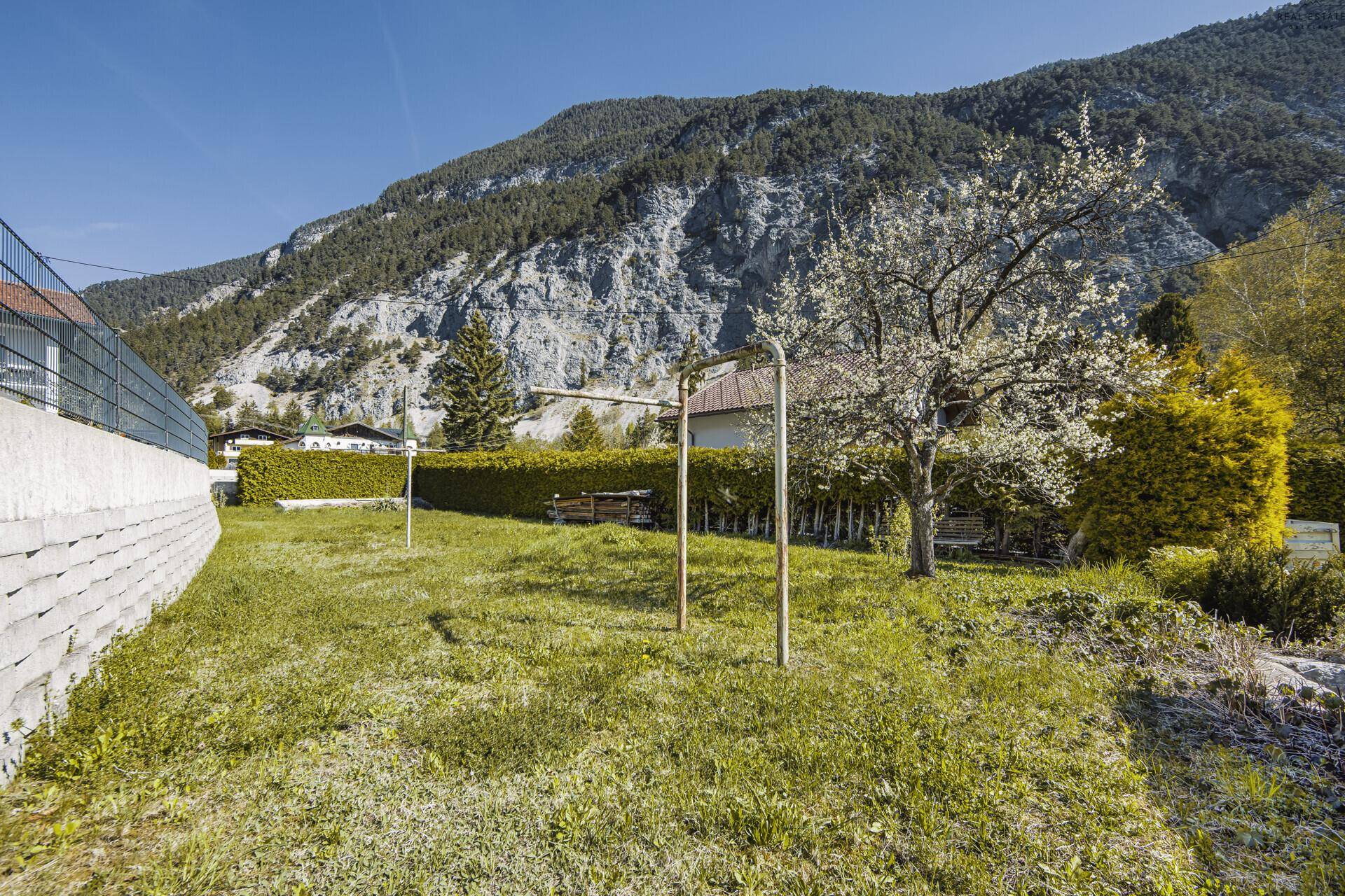 Grüner Gartenbereich mit Rasenfläche, Hecke und Blick auf die umliegenden Berge.