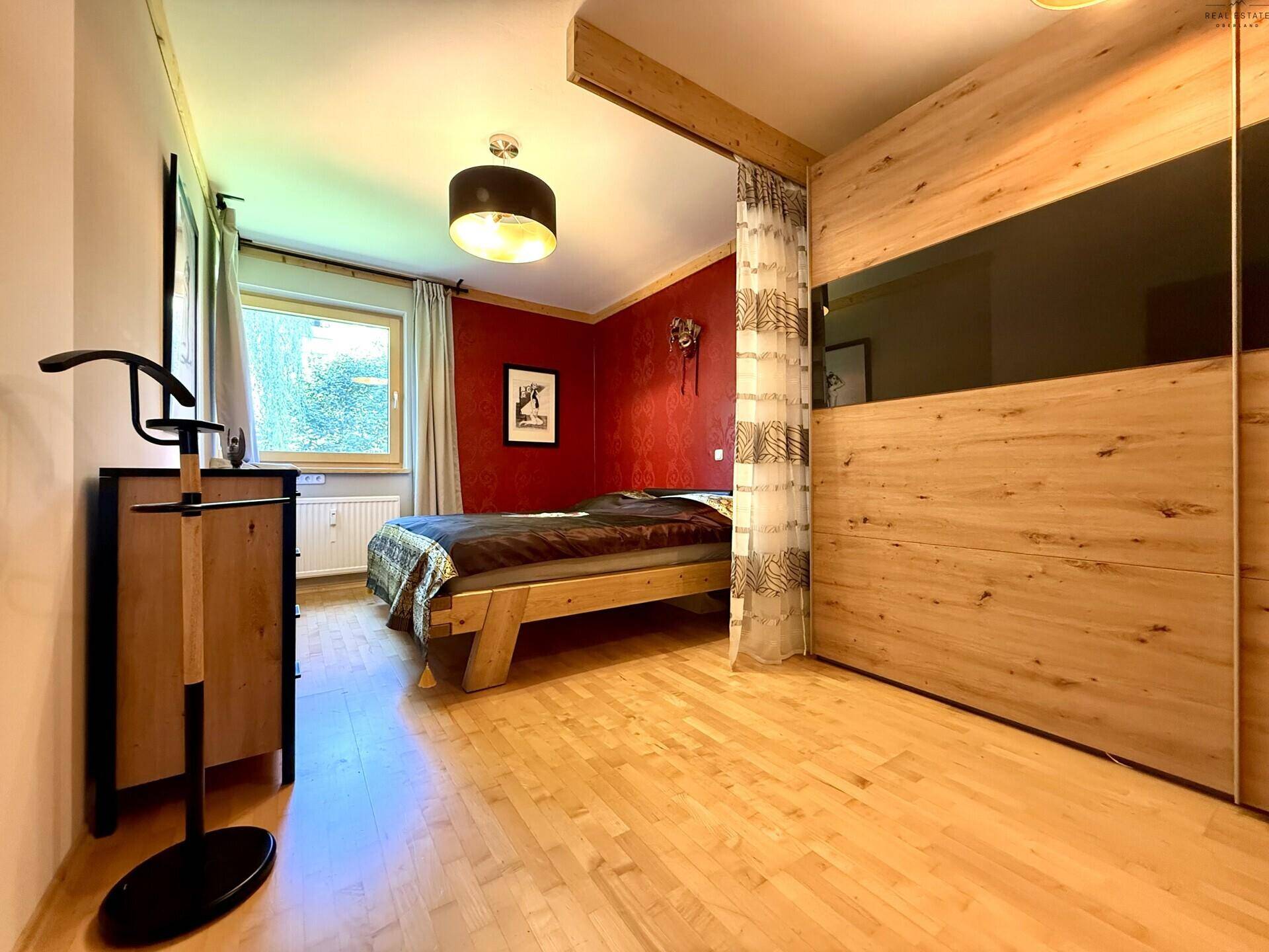 Schlafzimmer mit Holzbett, Schrank und roter Akzentwand.