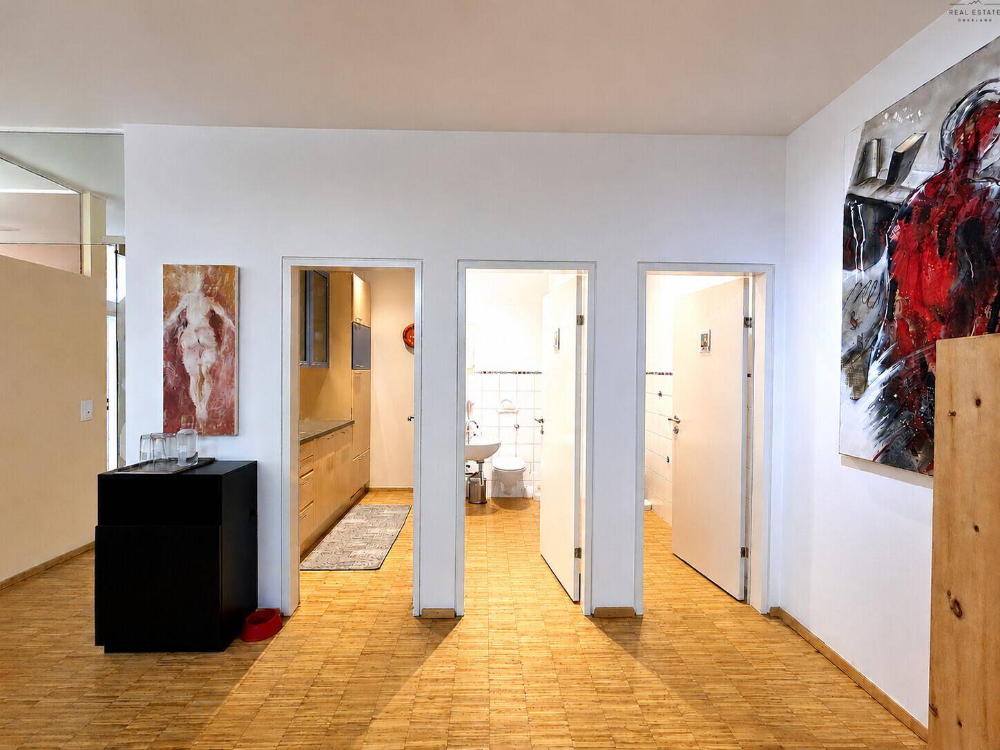 Flur mit drei offenen Türen, die zu einer Küchenzeile und zwei Badezimmern führen.