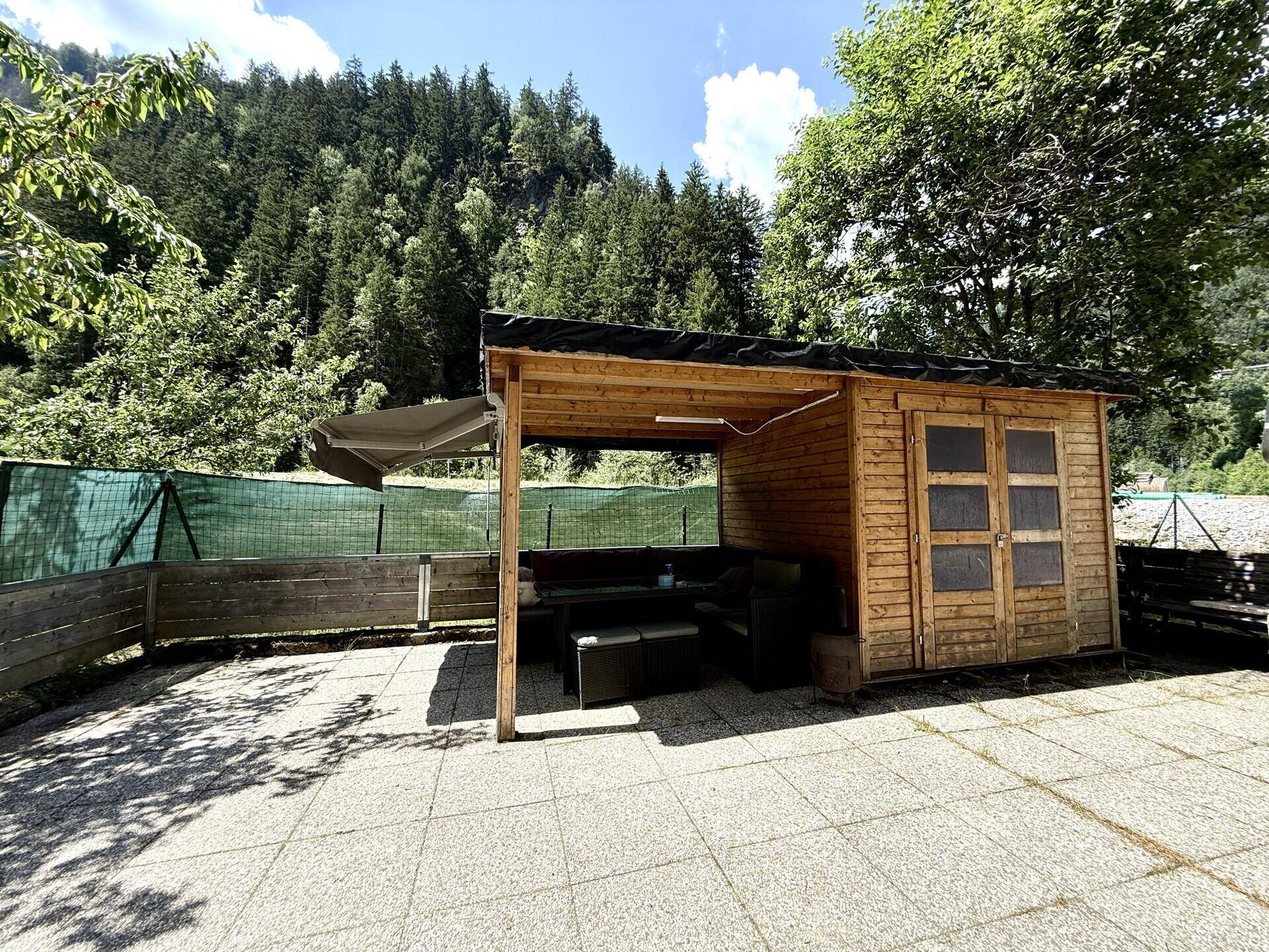 Großer Gartenbereich mit Holzschuppen und überdachtem Sitzbereich, umgeben von Natur.