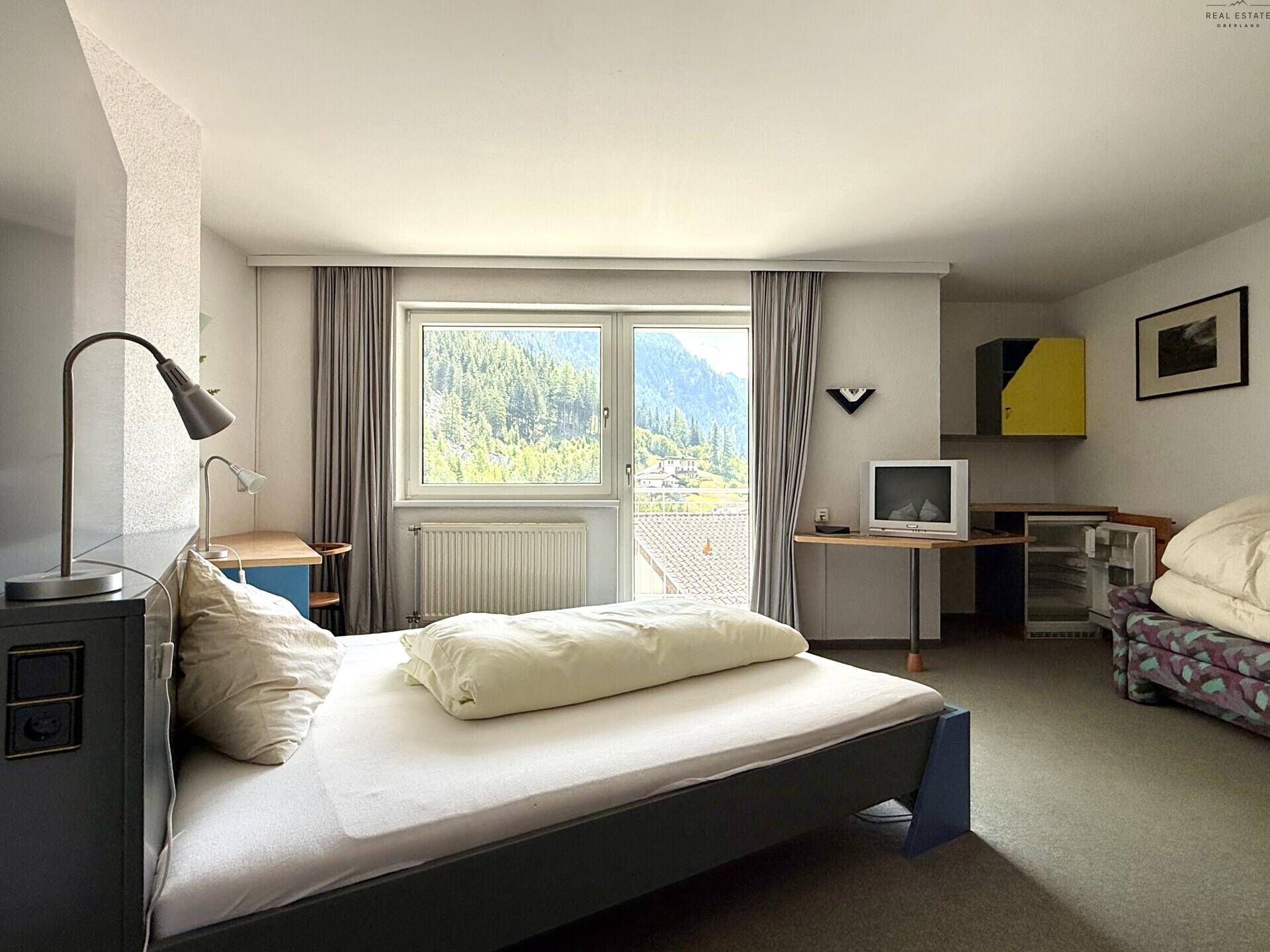 Schlafzimmer mit Bett, Fernseher und einem Fenster, das einen Blick auf die Berge bietet.
