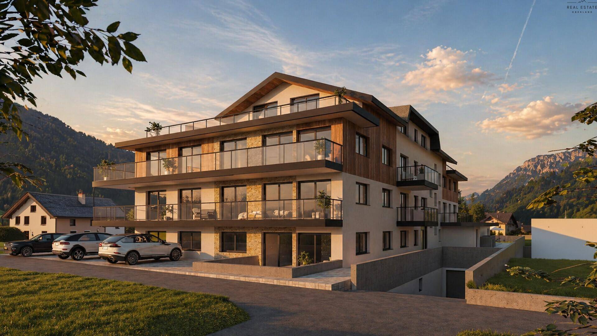 Moderne Wohnanlage mit Balkonen und Zufahrt zu einer Tiefgarage, umgeben von einer beeindruckenden Bergkulisse.