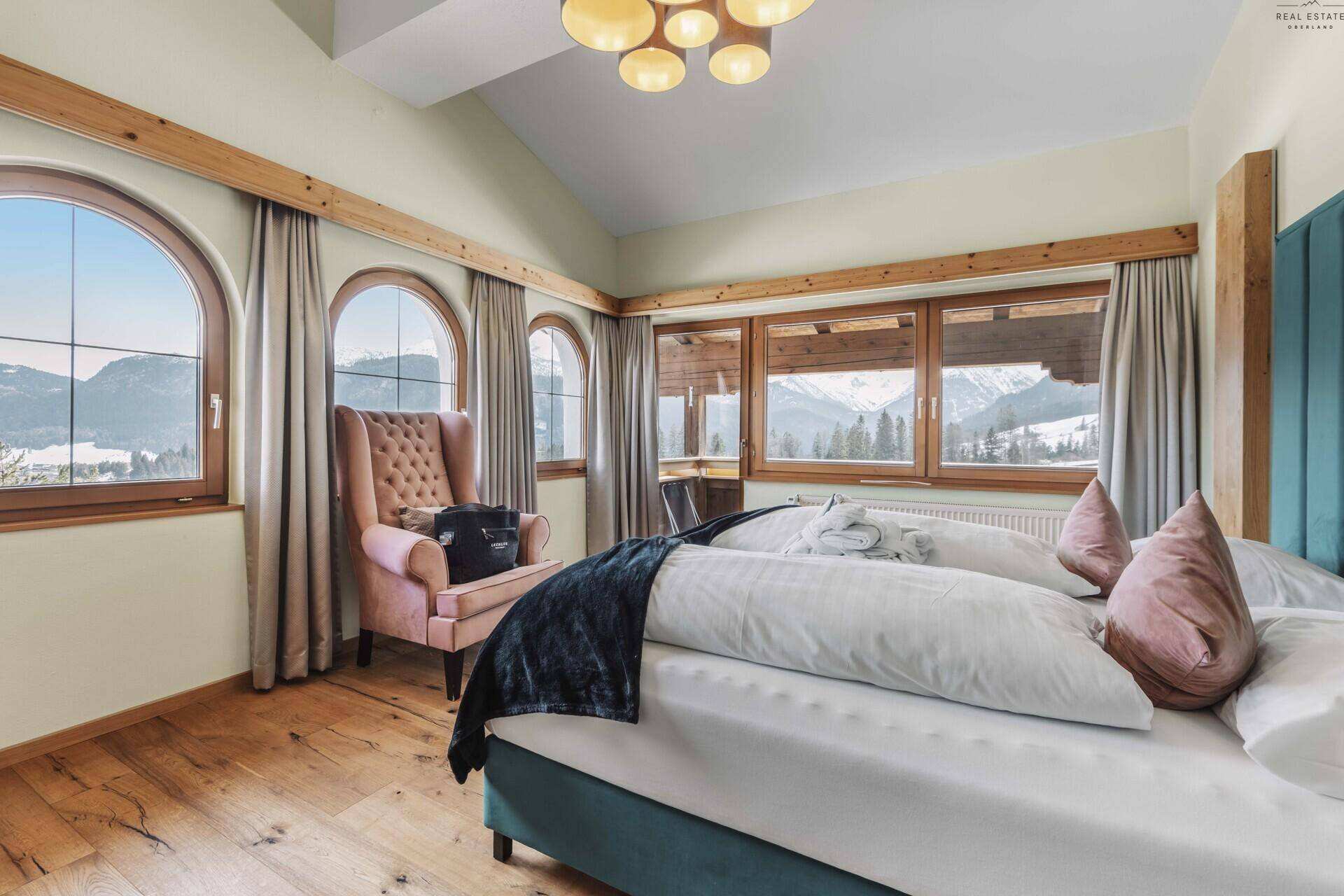 Helles Schlafzimmer mit Holzboden, großen Bogenfenstern und atemberaubendem Bergblick.