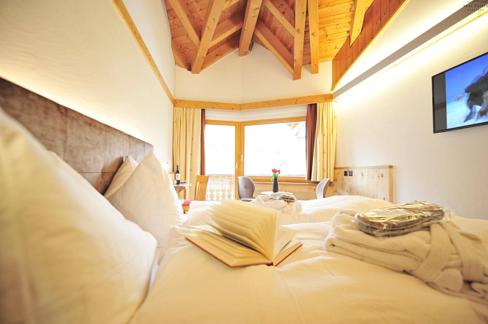 Helles Schlafzimmer mit Doppelbett, sichtbaren Holzbalken und einem Fenster mit Ausblick.