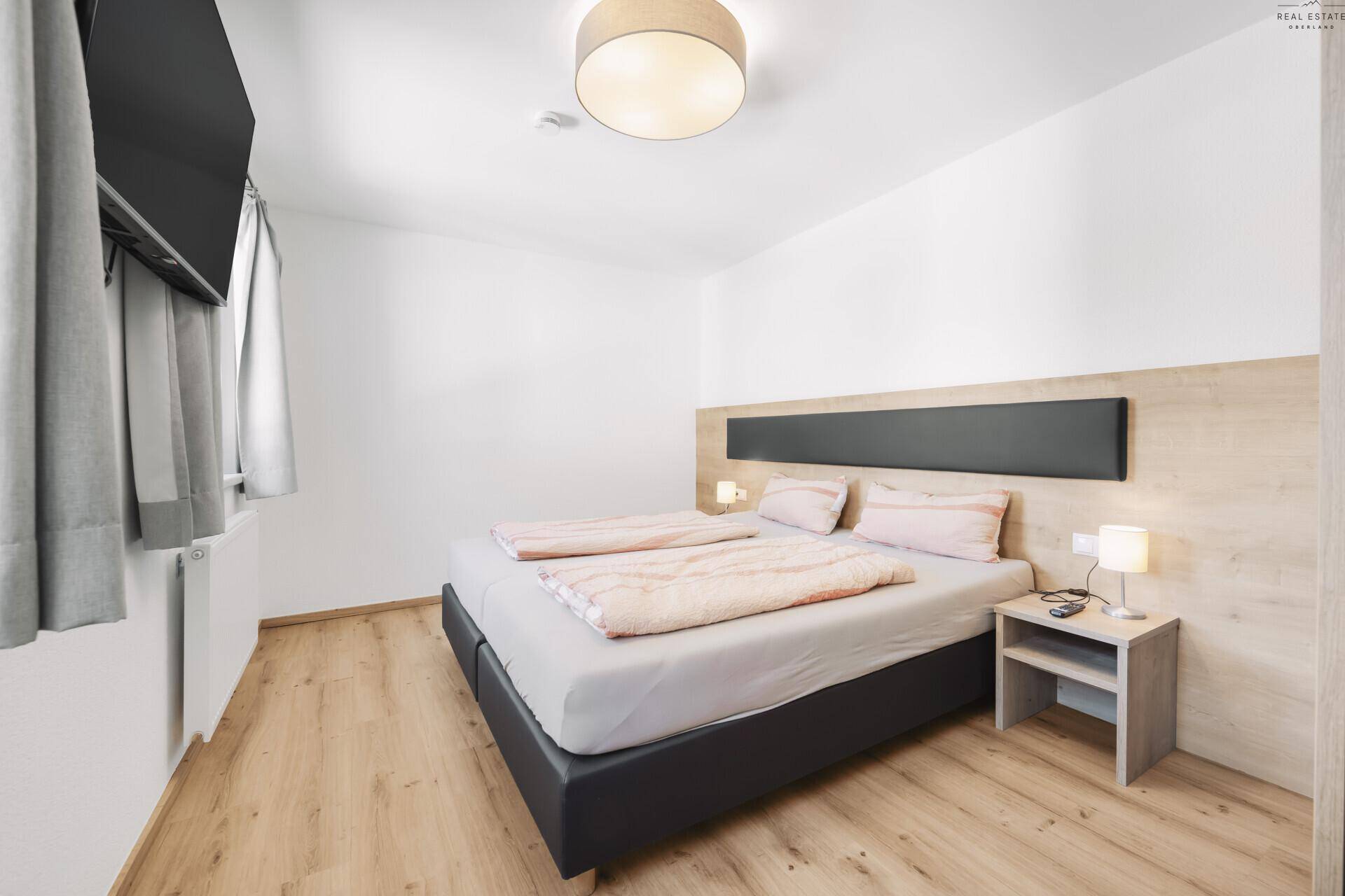 Helles Schlafzimmer mit Doppelbett, Holzboden und modernem Wandpaneel.