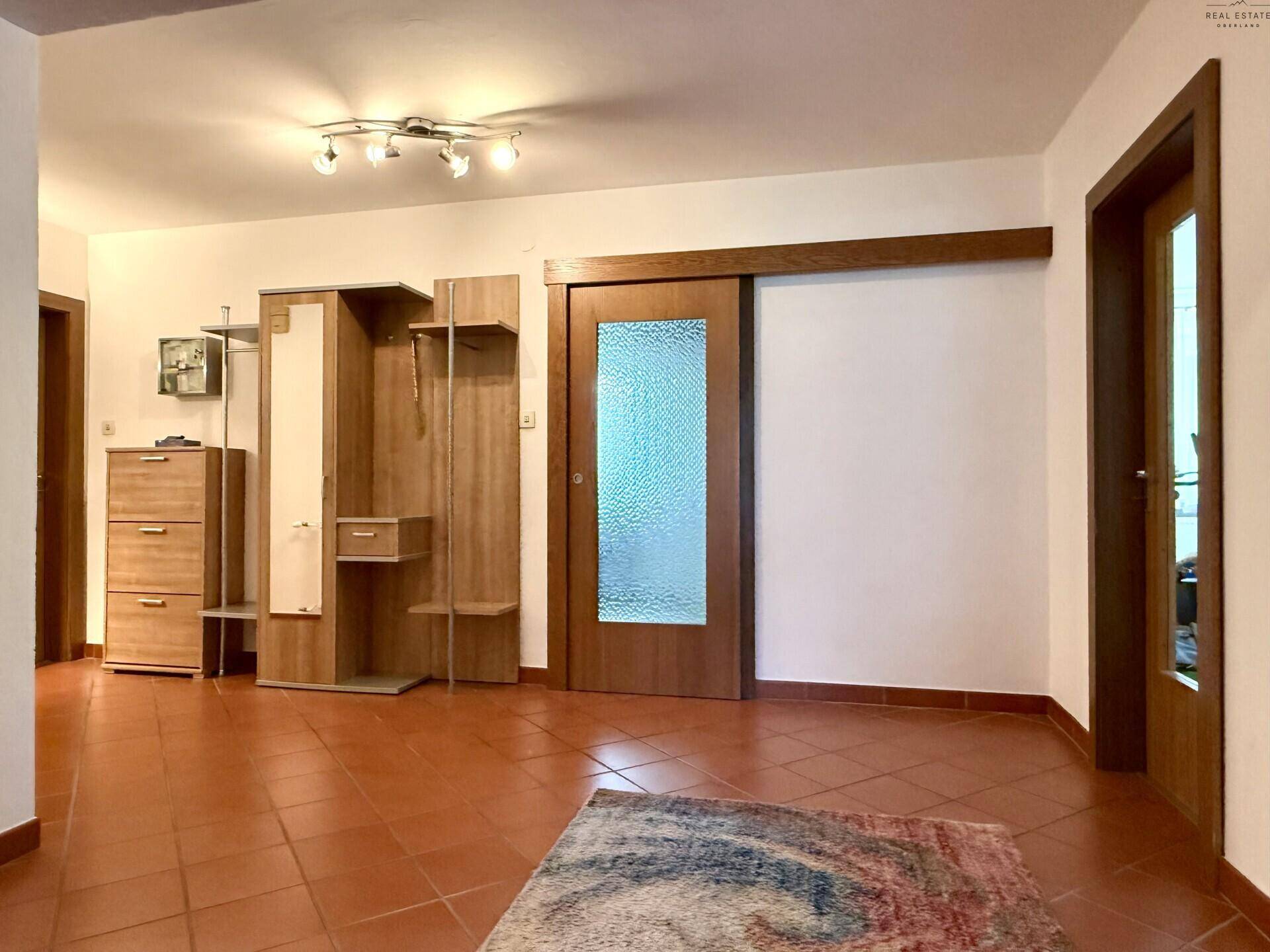 Geräumiger Flur mit Terrakotta-Fliesenboden, Garderobe und Schiebetür zu einem weiteren Raum.