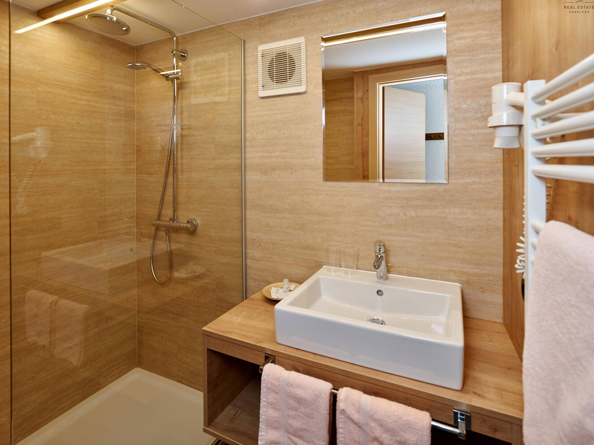 Modernes Badezimmer mit beigen Fliesen, Duschkabine und einem Waschbecken auf Holzunterschrank.