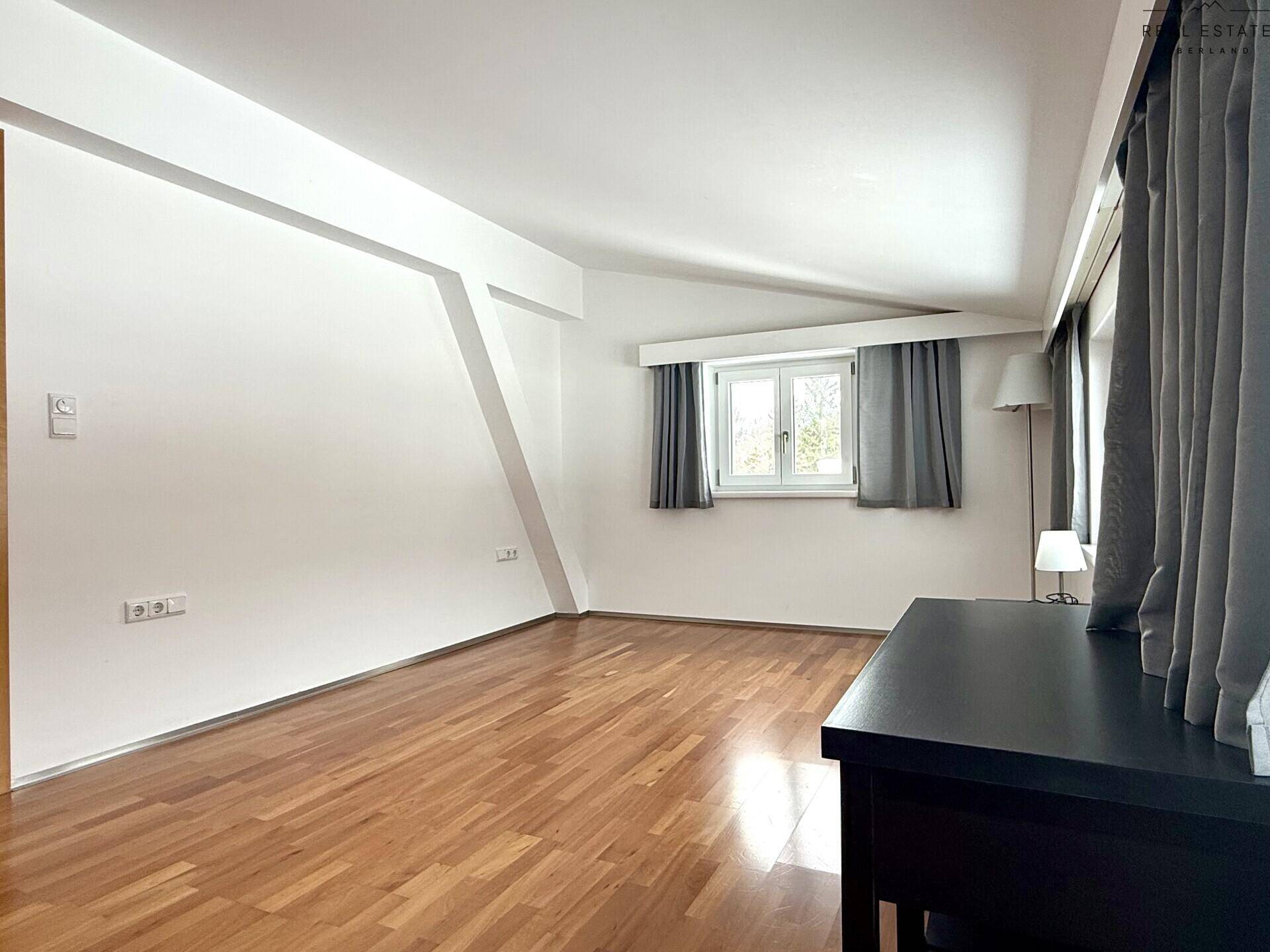 Helles Zimmer mit Holzfußboden, Fenster und Dachschrägen, bietet vielseitige Nutzungsmöglichkeiten.