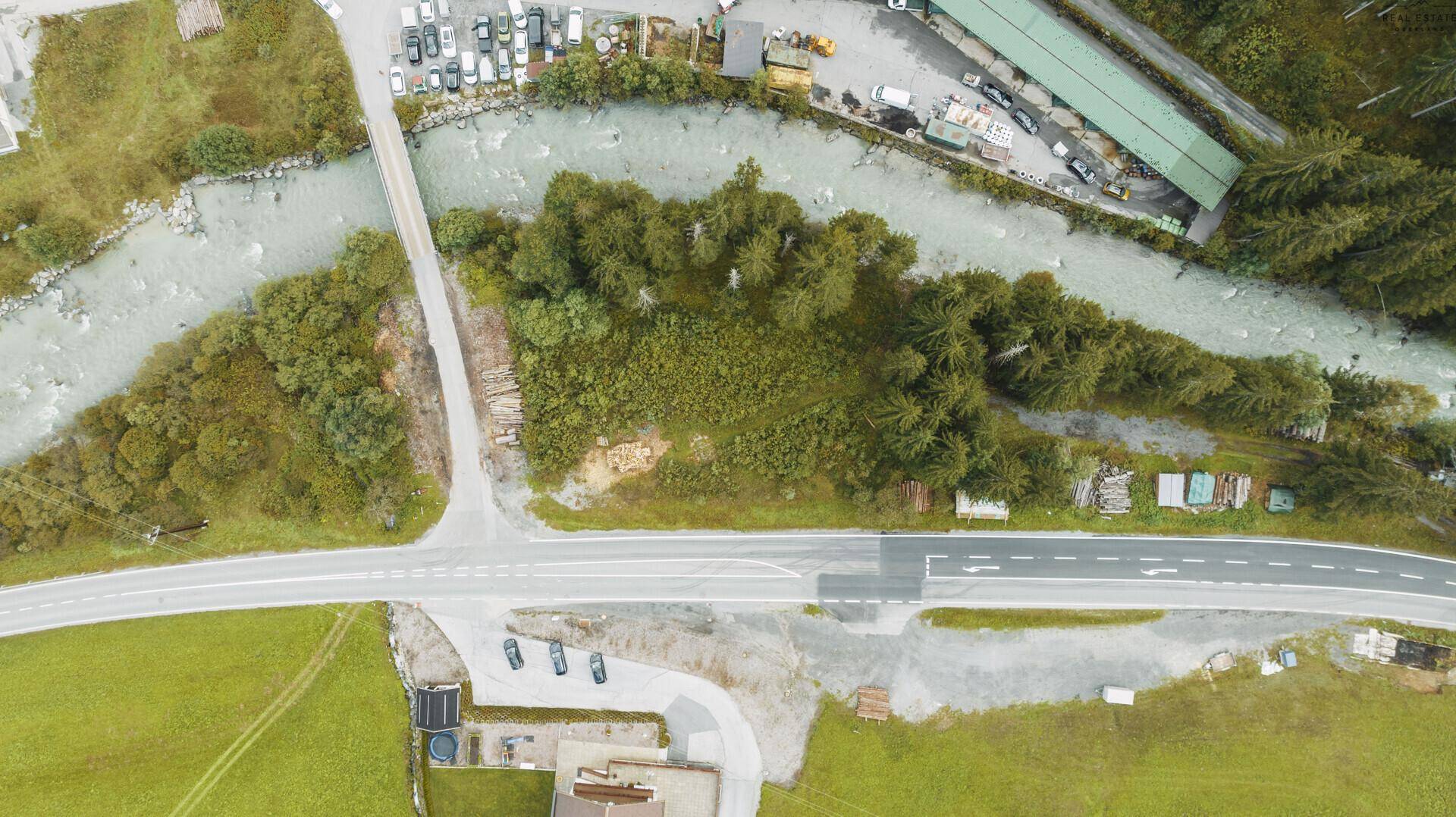 Senkrechte Luftaufnahme von Fluss, Brücke, Straße und angrenzenden grünen Flächen in einer Berglandschaft.
