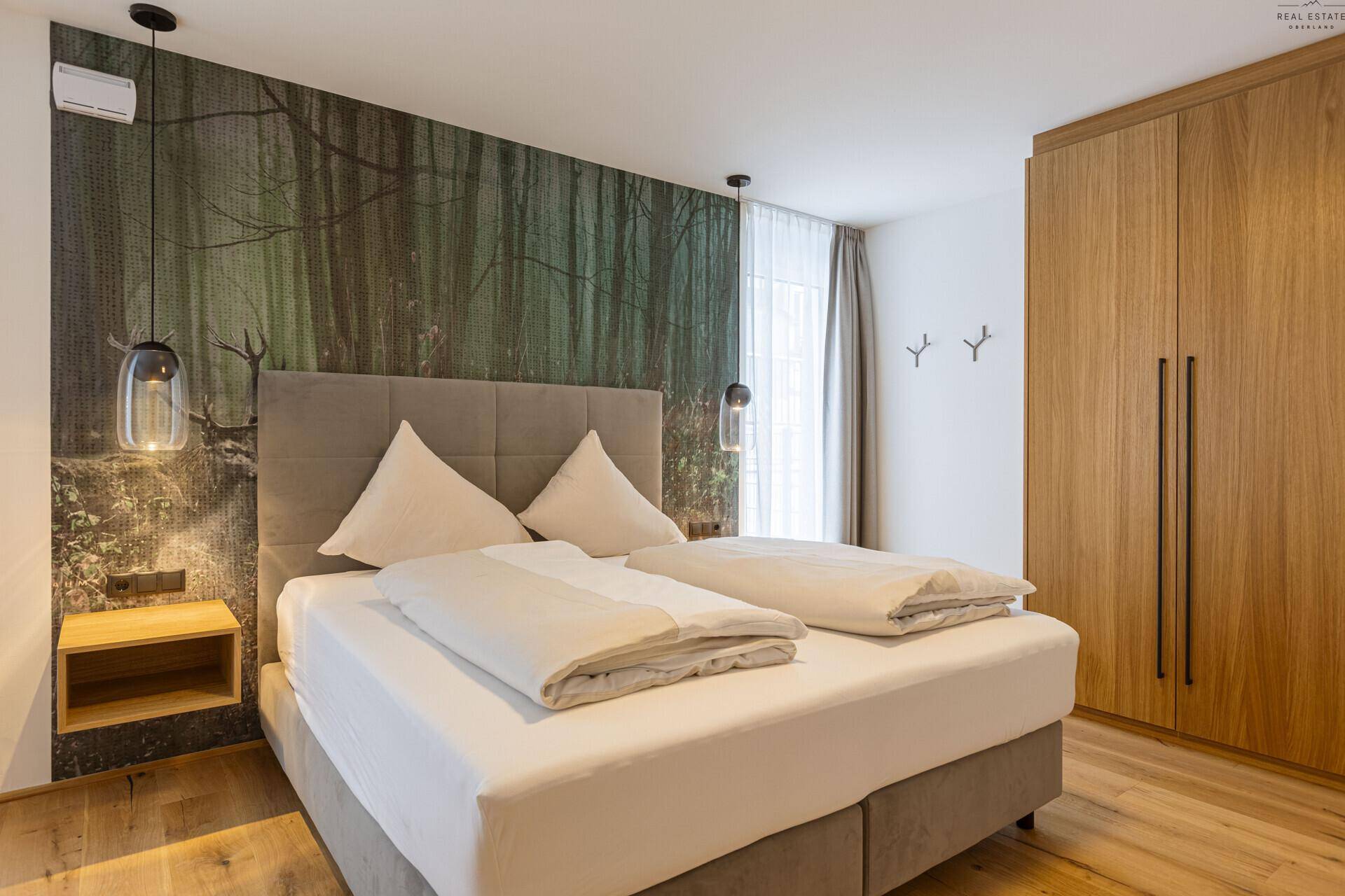 Schlafzimmer mit Doppelbett, Holzboden und einer Waldmotiv-Tapete als Akzentwand.