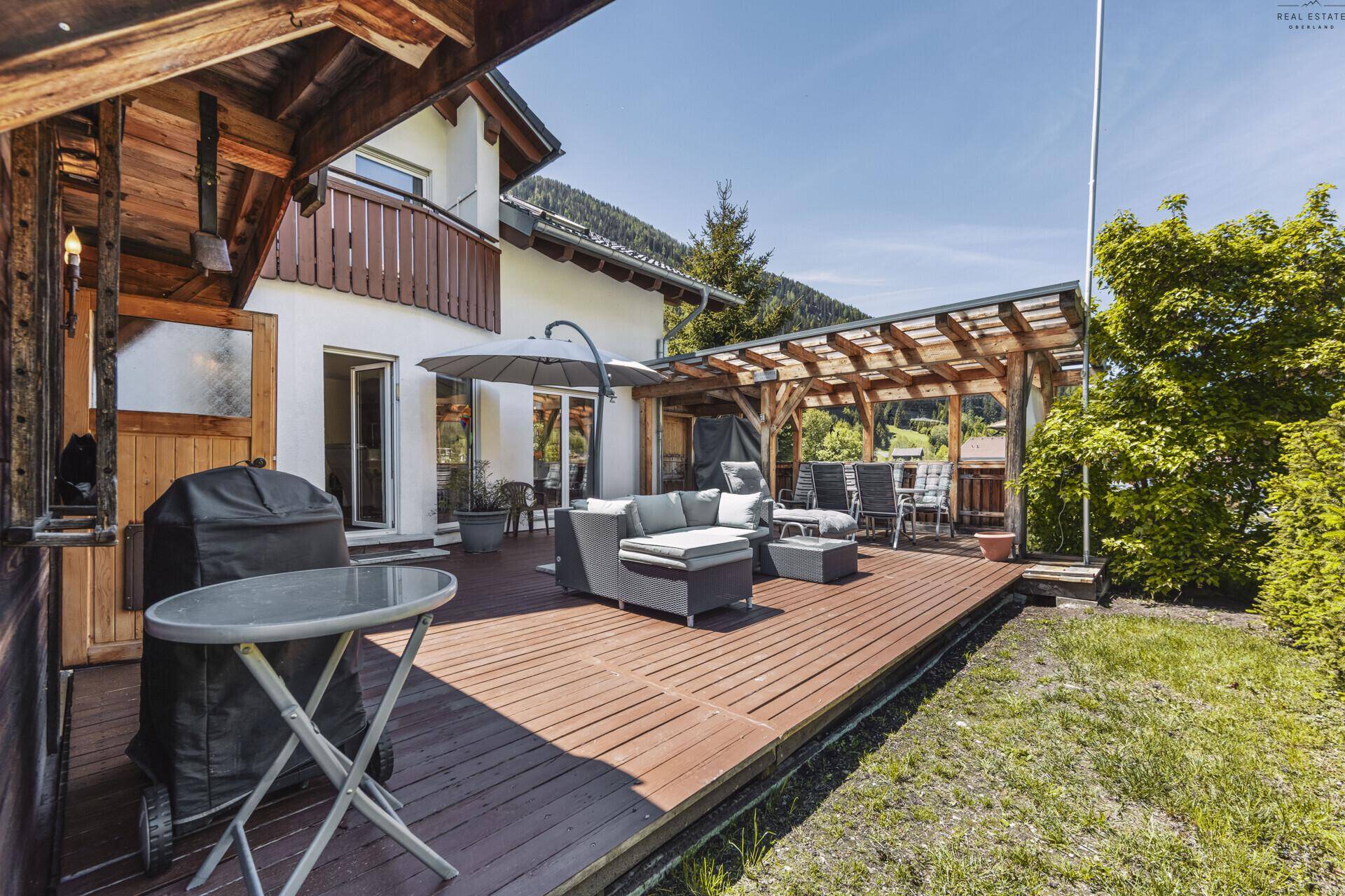 Große Holzterrasse mit Lounge-Bereich, Grill und überdachtem Essplatz im Freien.