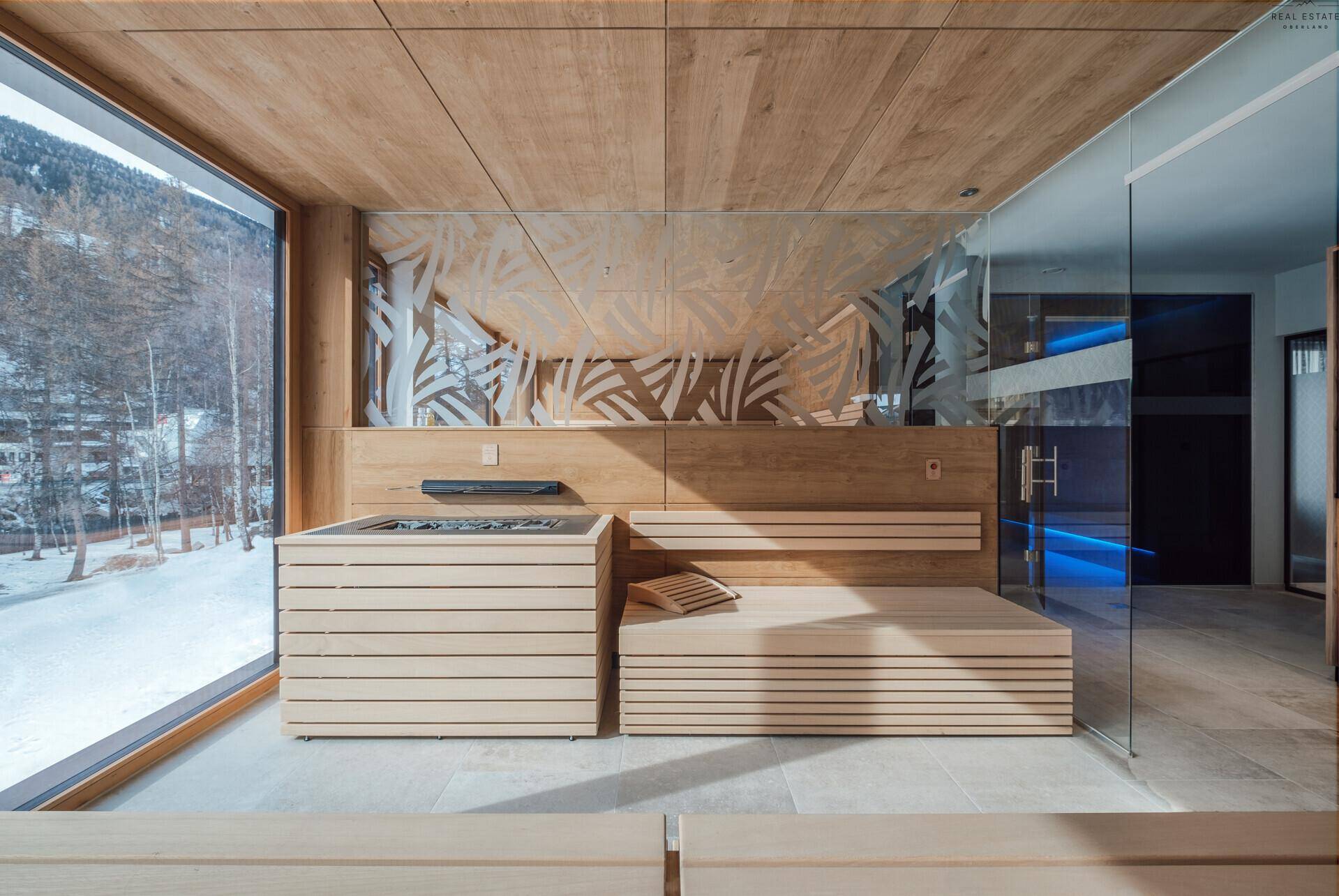 Geräumige Sauna mit großen Fenstern, Holzverkleidung und Blick auf die verschneite Winterlandschaft.