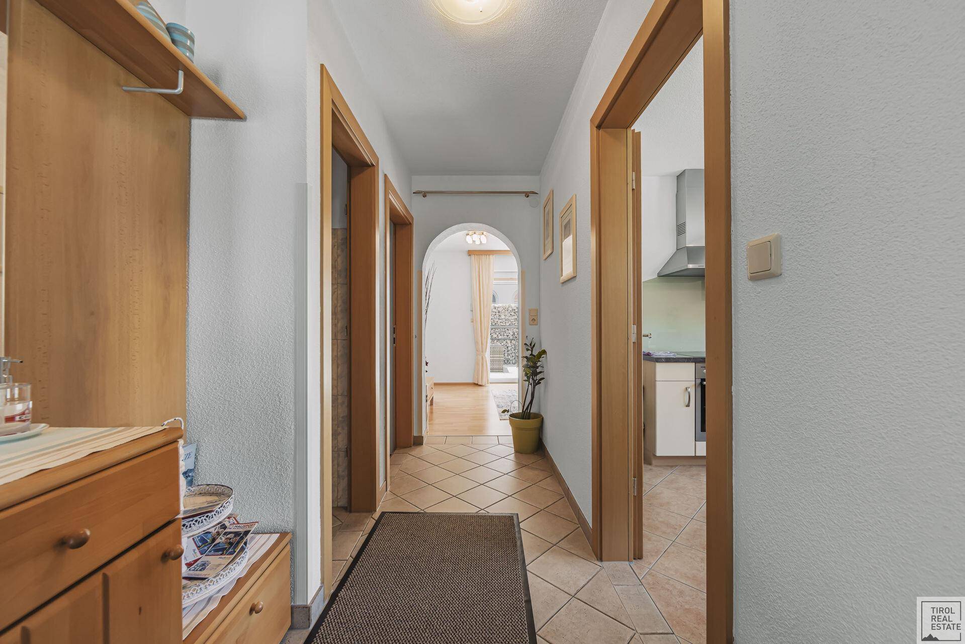 Heller Flur mit beigefarbenen Fliesen, Holztüren und Garderobe, der zu weiteren Räumen führt.