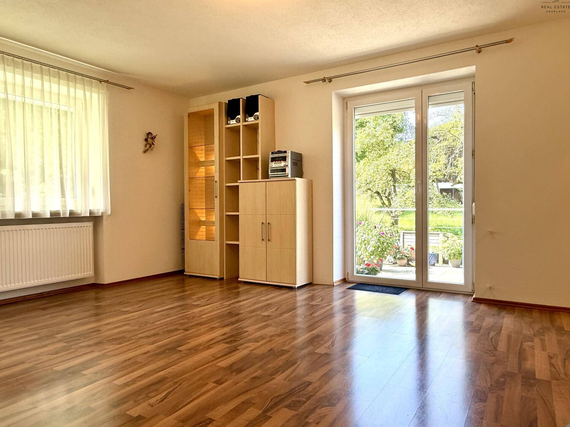 Helles Wohnzimmer mit Laminatboden und direktem Zugang zum Garten durch eine Glastür.