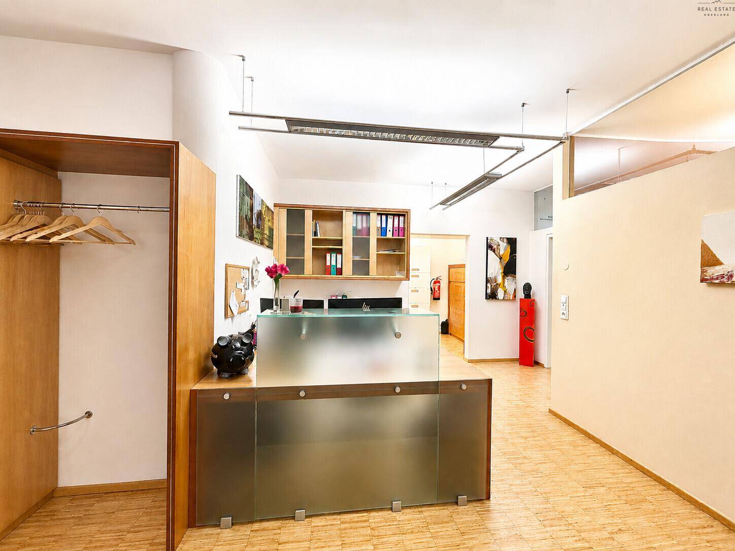 Moderner Empfangstresen mit Milchglasfront, Garderobe und Holzschränken in einem Büro.