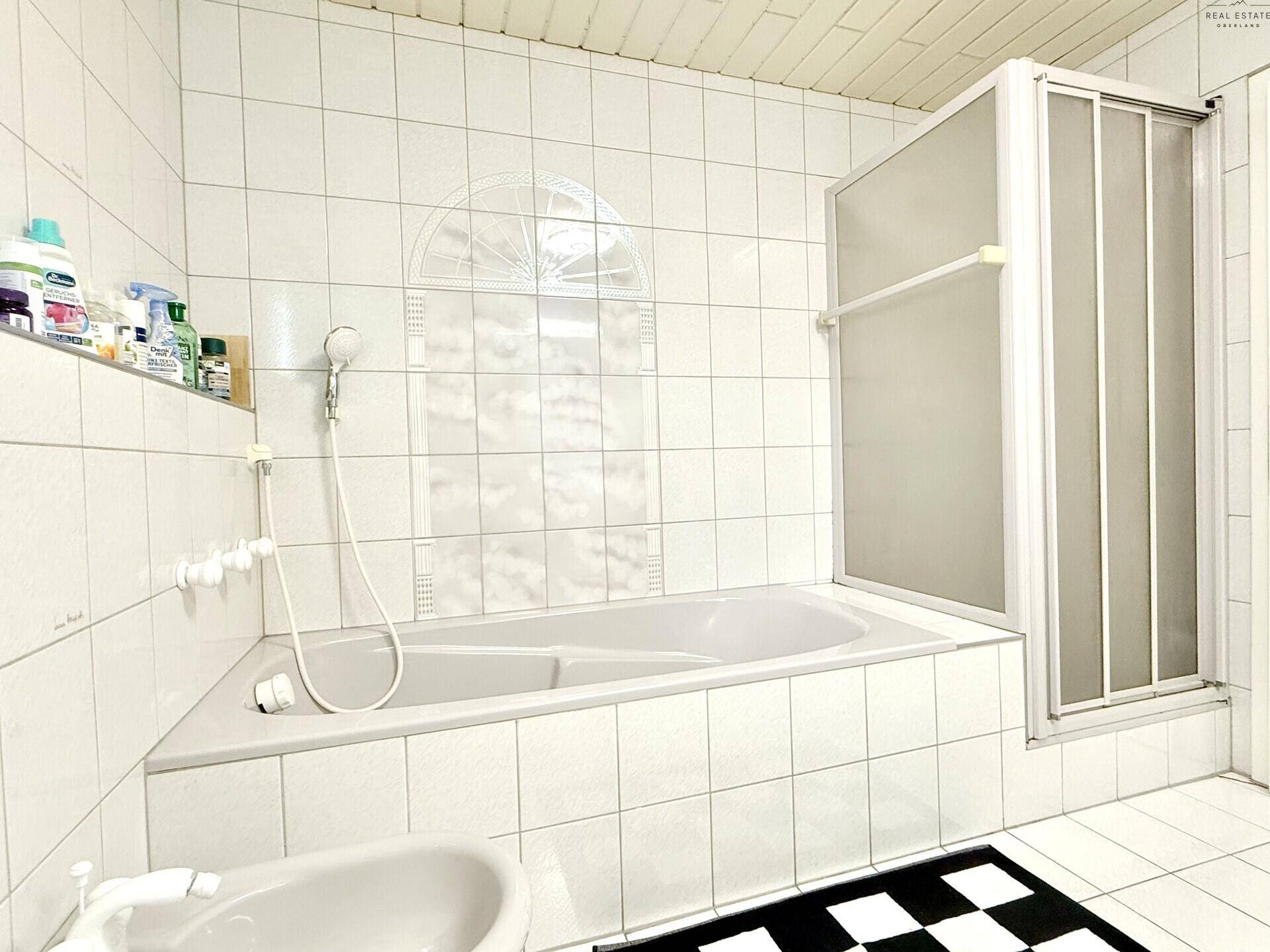 Badezimmer mit Badewanne, Duschabtrennung und weißen Fliesen.