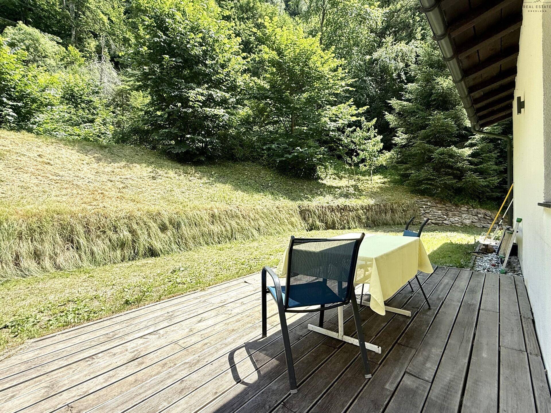 Holzterrasse mit Sitzgelegenheiten und Blick auf die grüne Umgebung und den Wald.