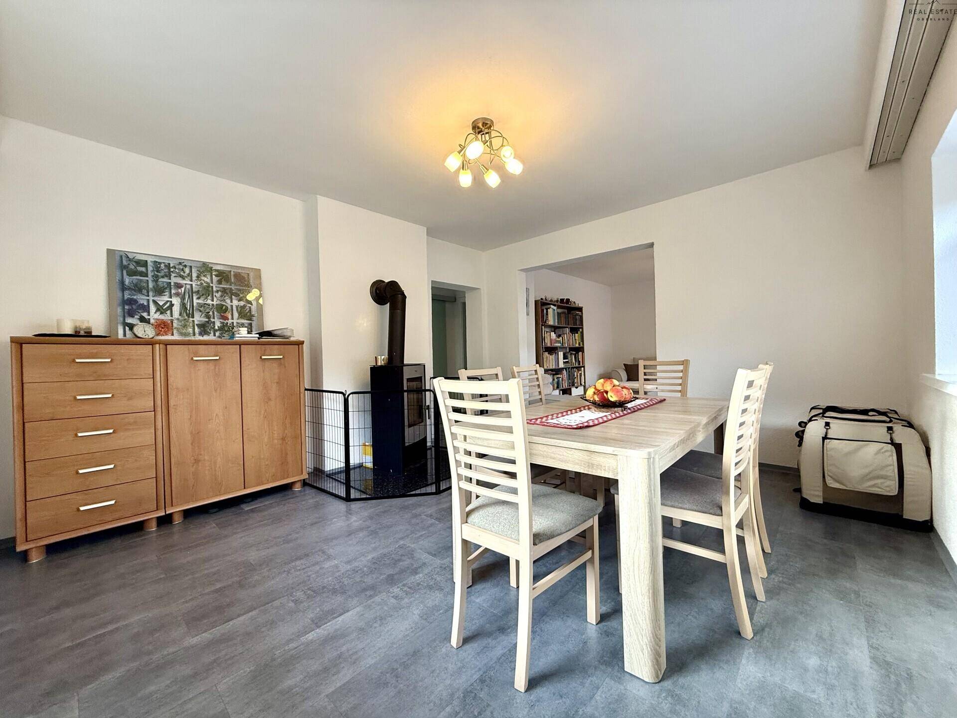Essbereich mit Holztisch, Sideboard und Kaminofen im Hintergrund.