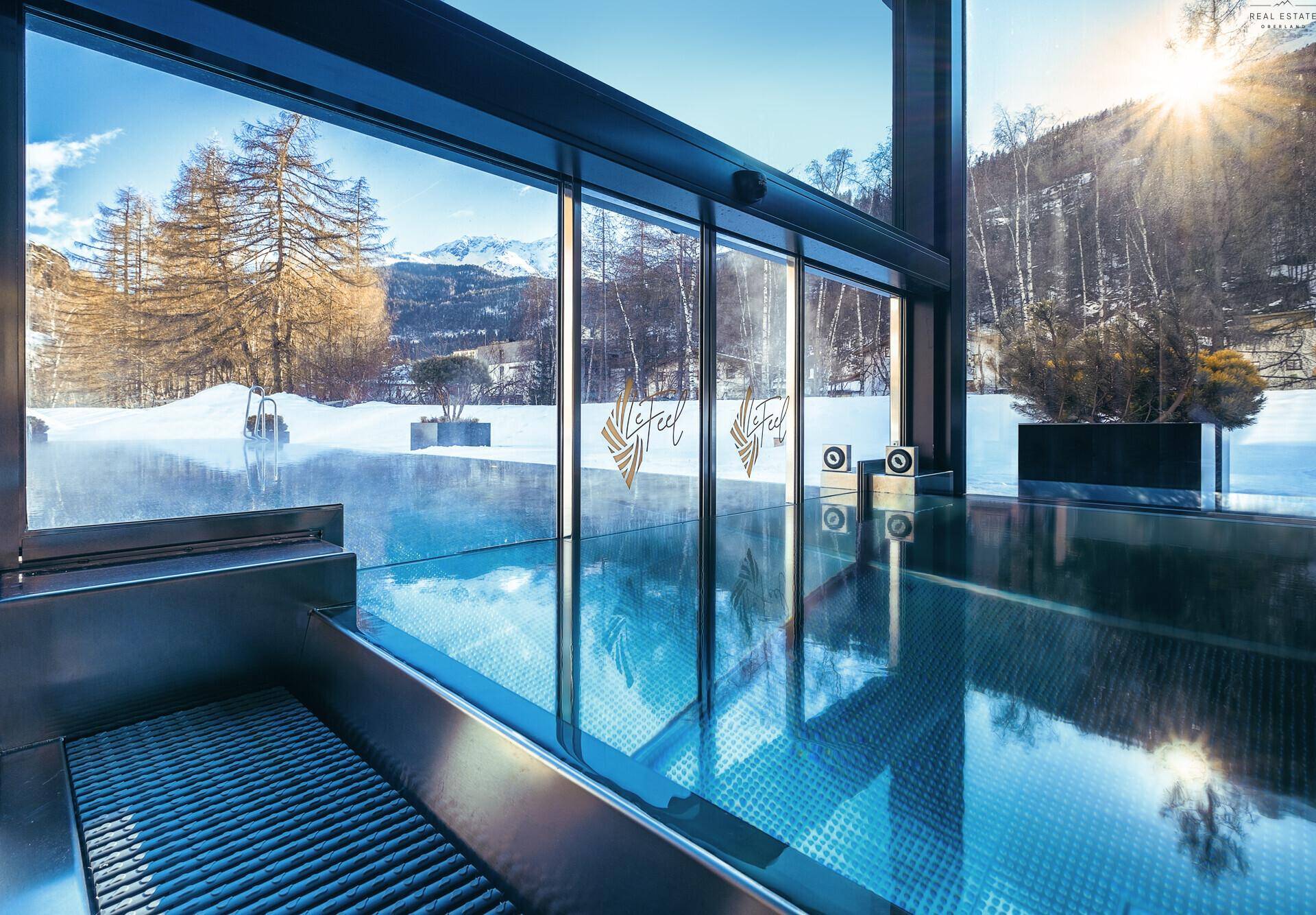 Heller Innenpool mit großen Glasfronten, die einen weiten Blick auf die verschneite Berglandschaft bieten.