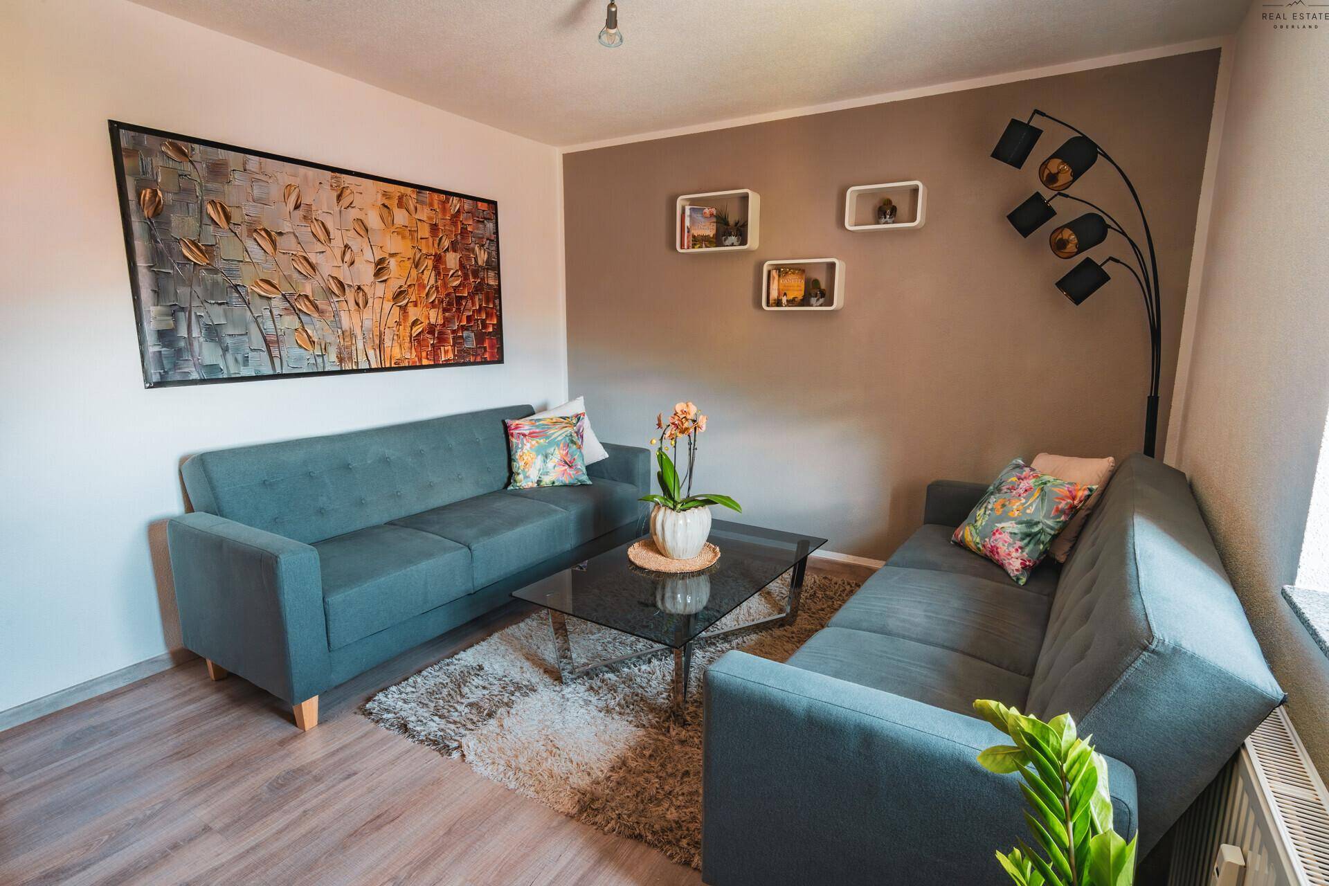 Wohnzimmer mit bequemen Sofas, Kunst an der Wand und Teppich auf Laminatboden.