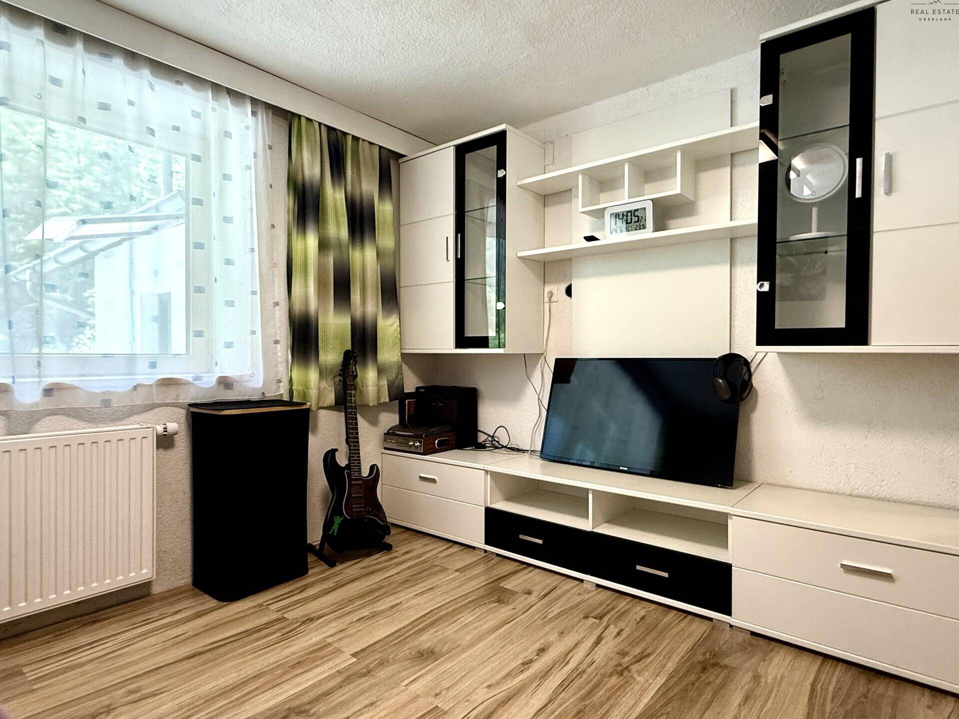 Wohnbereich mit TV-Möbeln, Holzfußboden und Fenster mit Blick nach draußen.