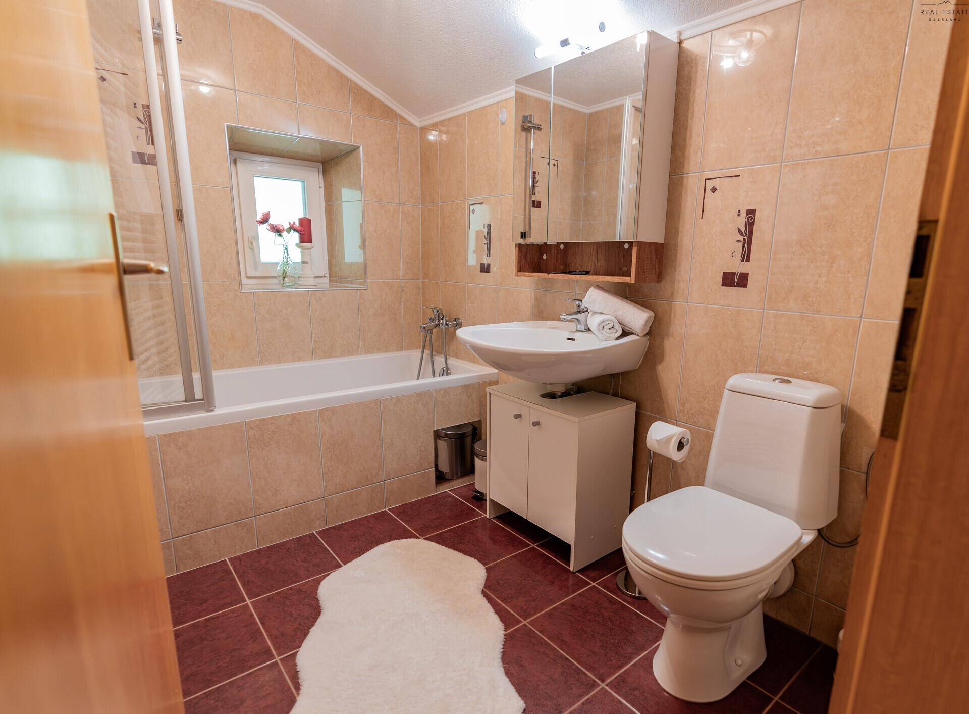 Badezimmer mit Badewanne, Waschbecken, WC und beigefarbenen Fliesen an Wänden und Boden.