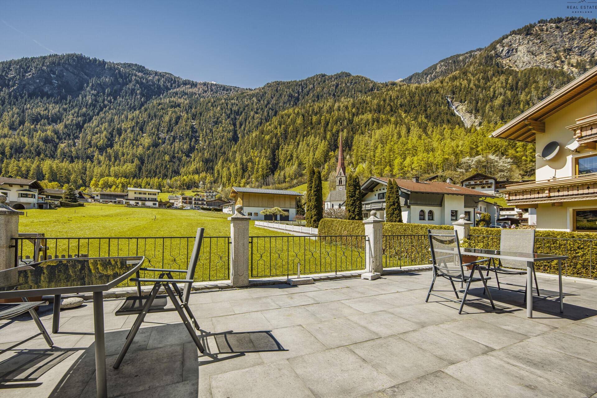 Große Steinterrasse mit Sitzgelegenheiten und Blick auf ein Dorf und die Berge.