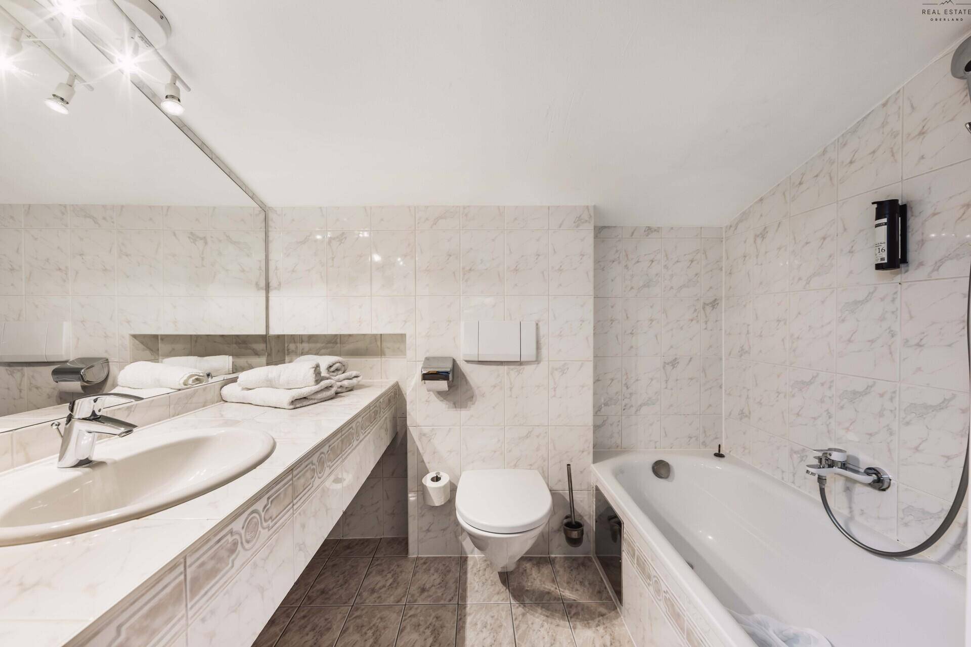 Helles Badezimmer mit Badewanne, Waschtisch und hellen Fliesen.