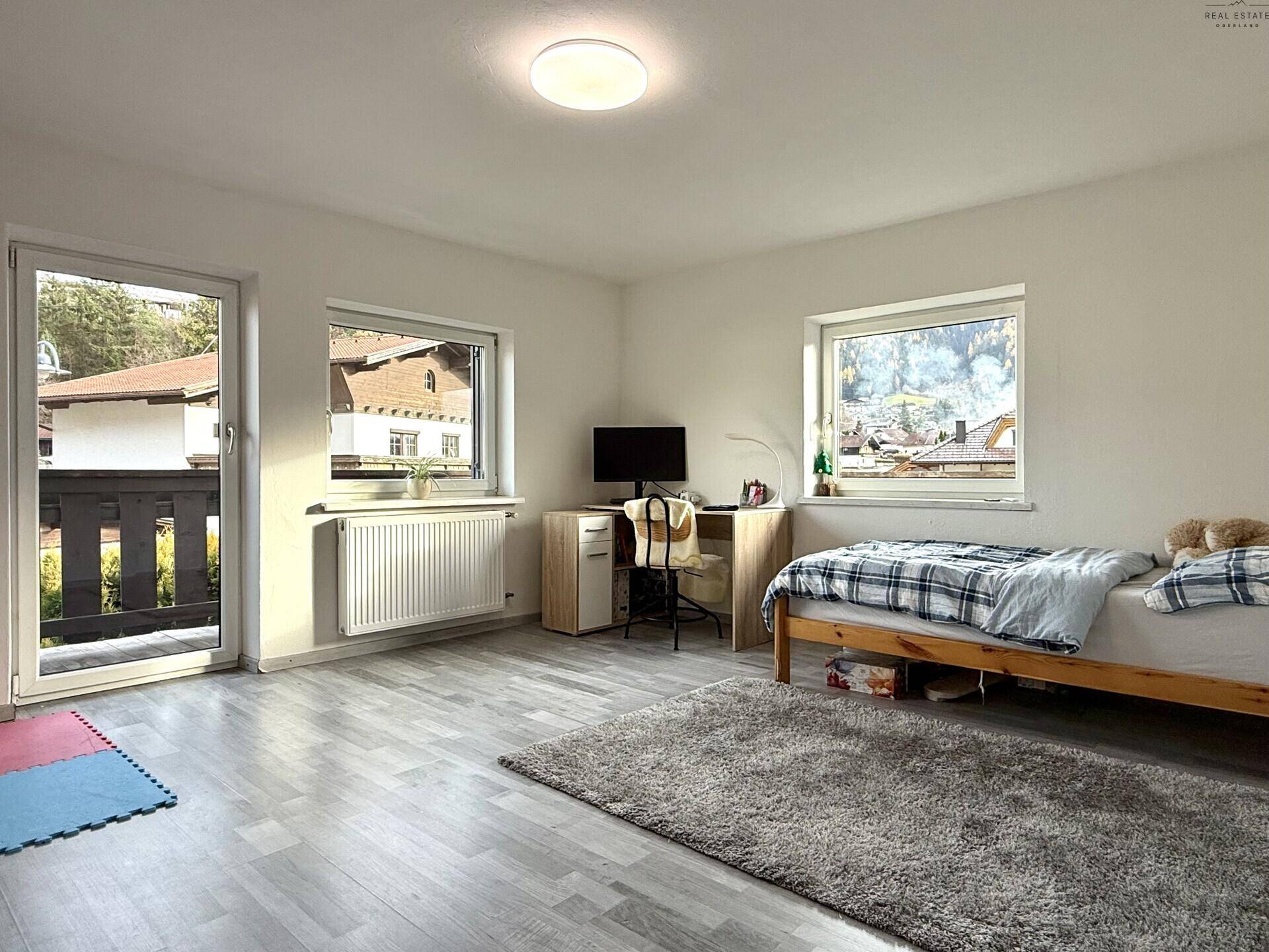Kinderzimmer mit Bett, Schreibtisch und Zugang zum Balkon.