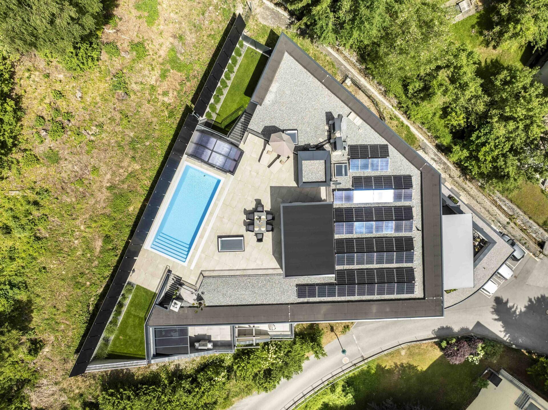 Vogelperspektive des einzigartigen Anwesens mit dreieckigem Grundriss, großem Pool und zahlreichen Solarpaneelen.