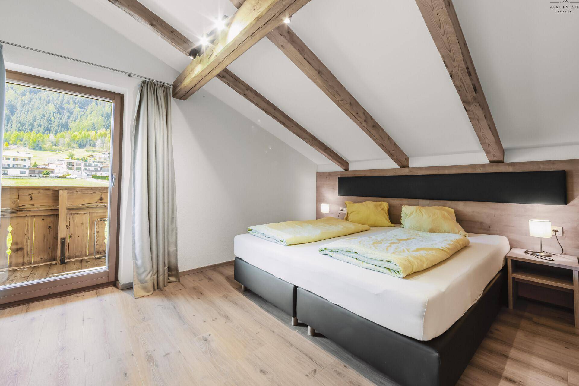 Helles Schlafzimmer im Dachgeschoss mit Holzbalken, Doppelbett und Balkonzugang.