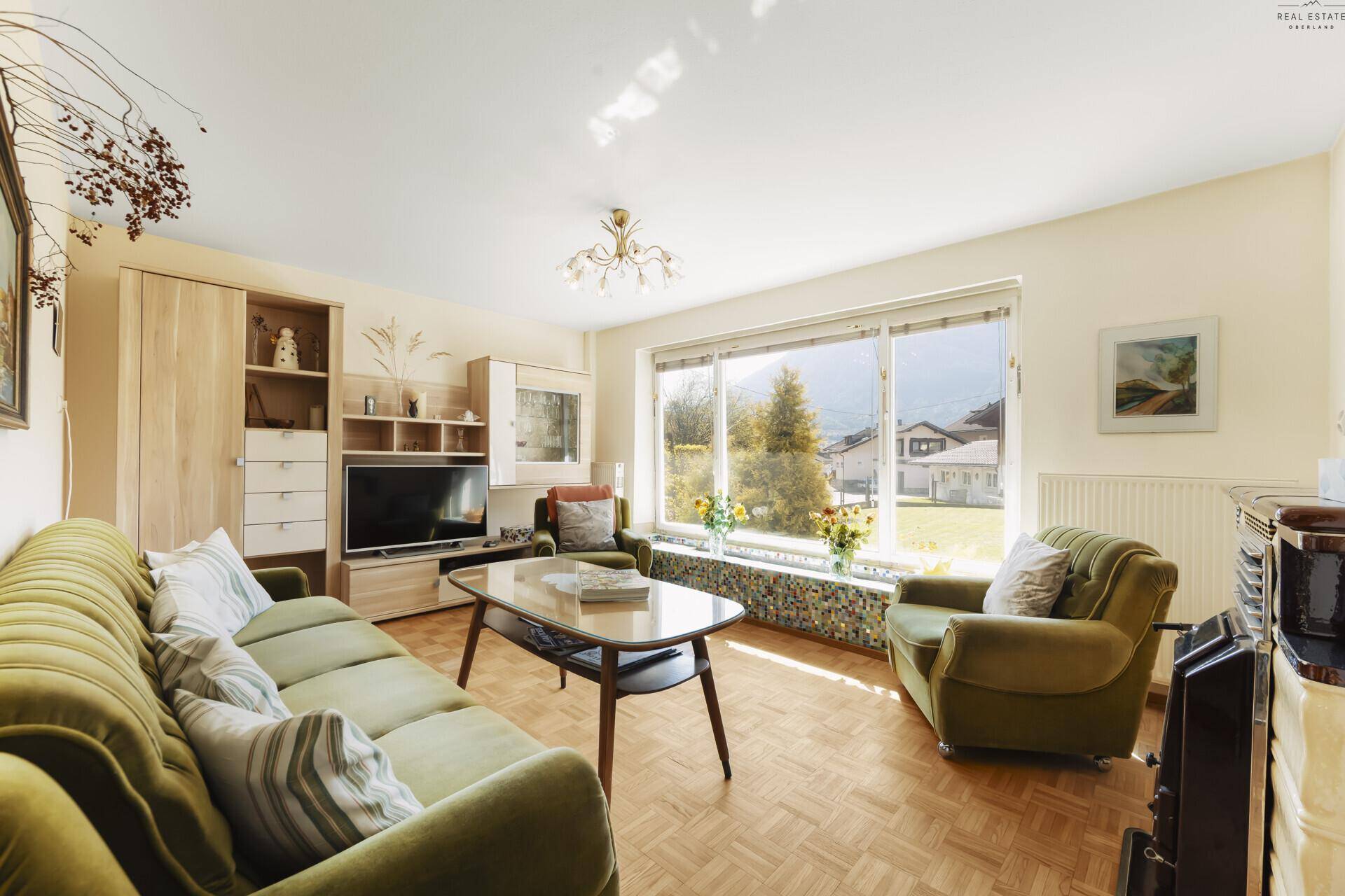 Helles Wohnzimmer mit bequemen Sofas, Parkettboden und großem Fenster mit Bergblick.