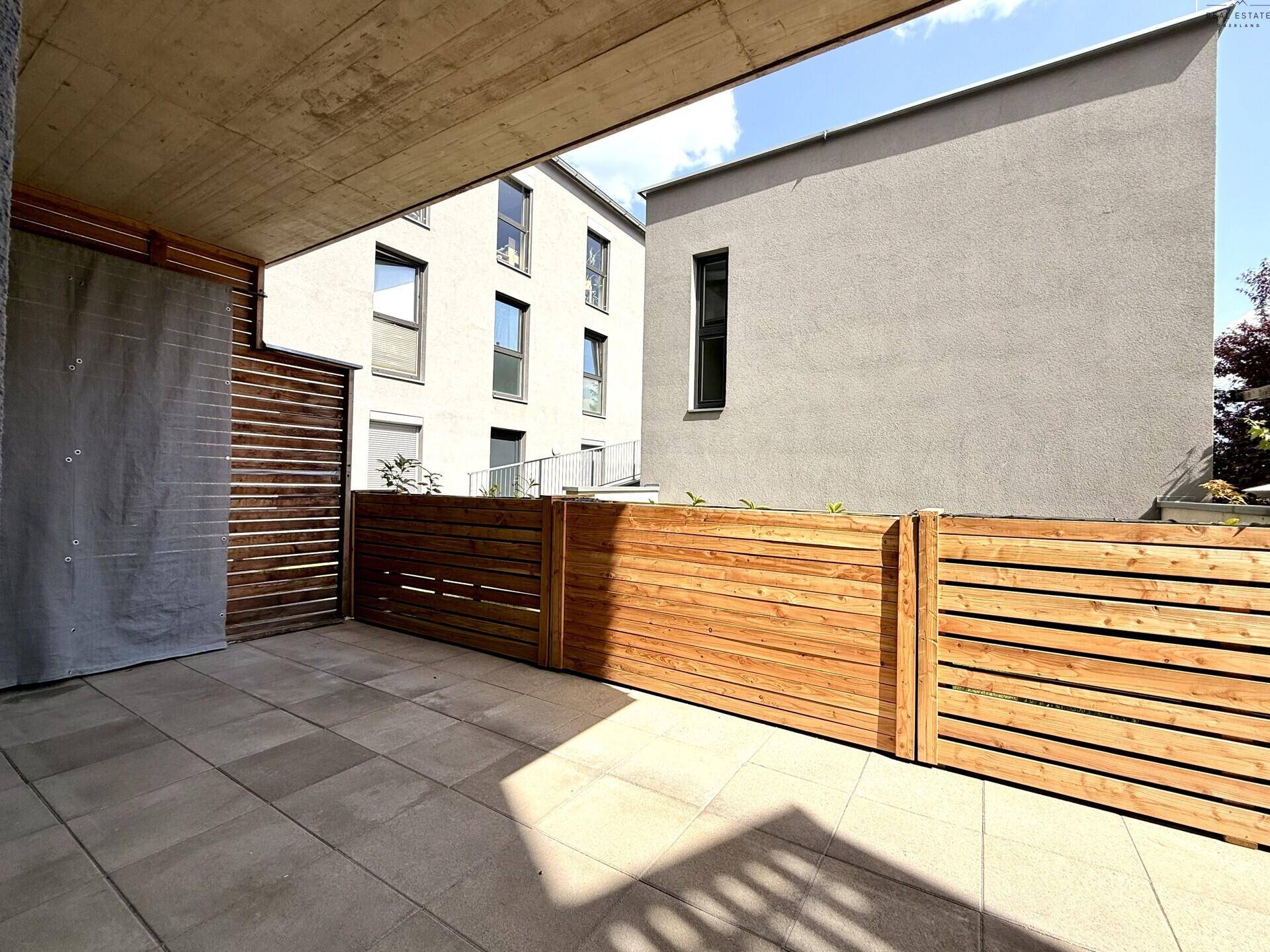 Terrasse mit Holzzaun und Blick auf die moderne Gebäudefassade bei Sonnenschein.