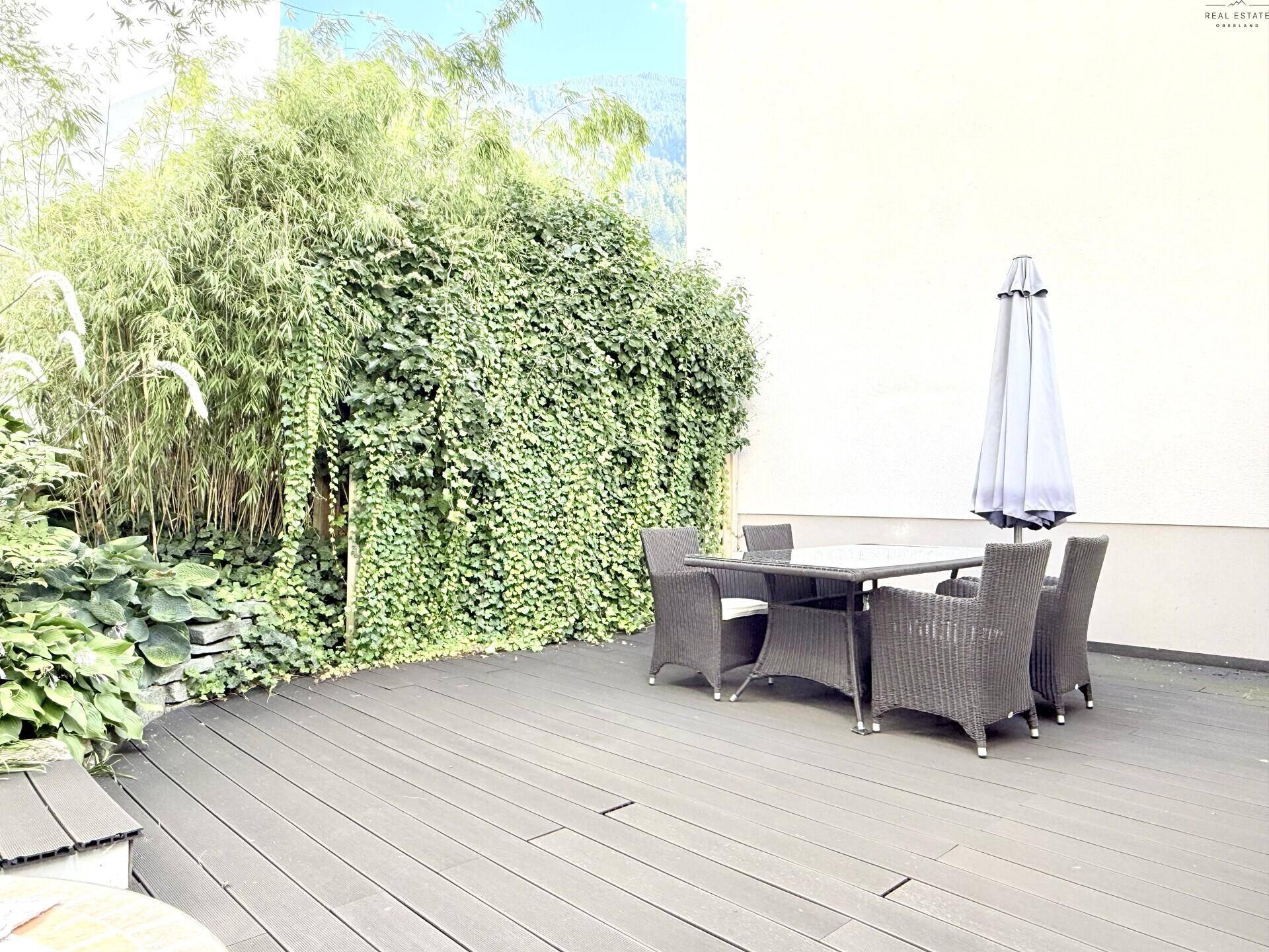 Terrasse mit üppiger Begrünung, dunklem Holzboden und Sitzbereich.