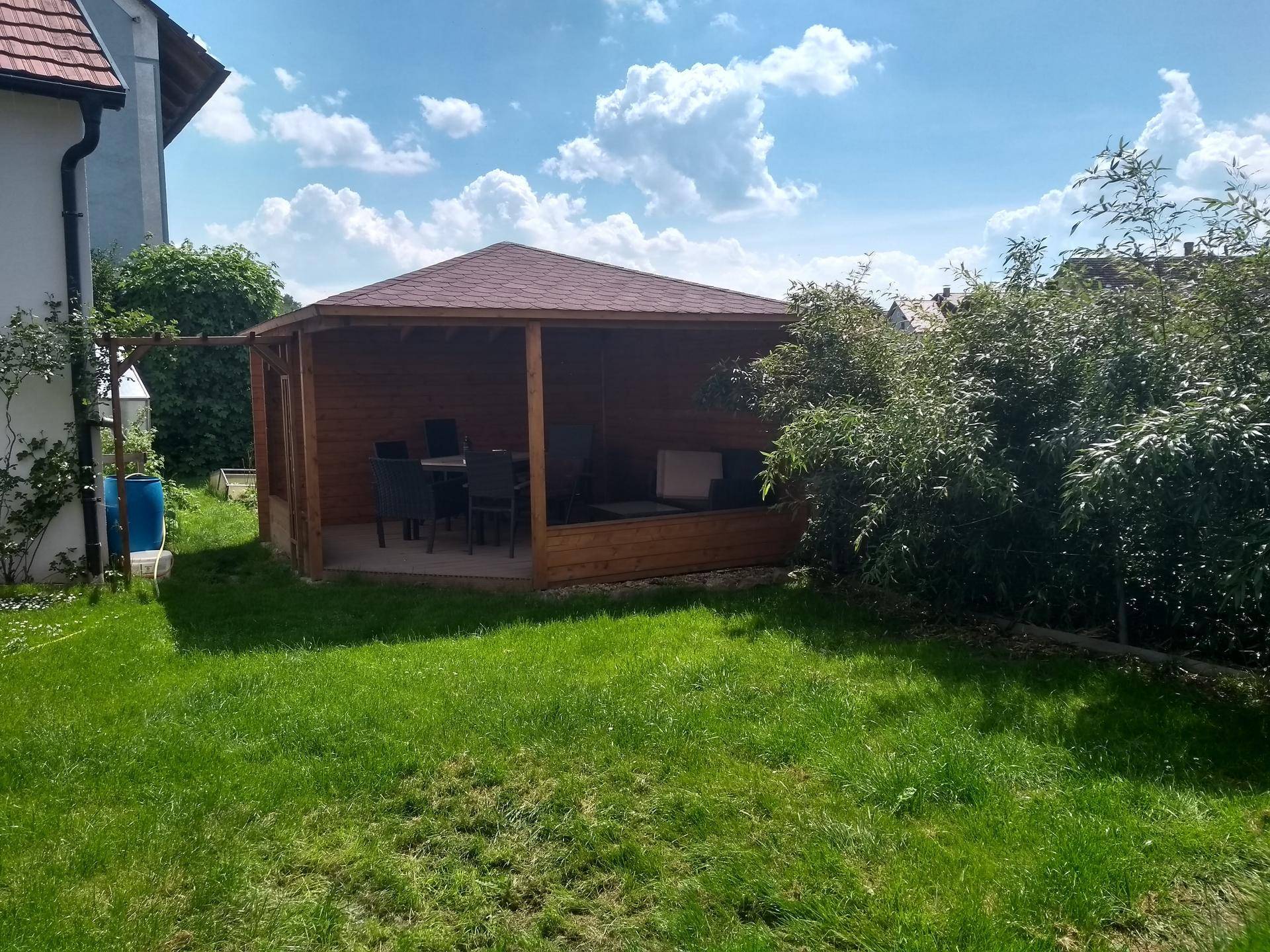 Geräumiger Holzpavillon mit Sitzgelegenheiten in einem grünen Gartenbereich.