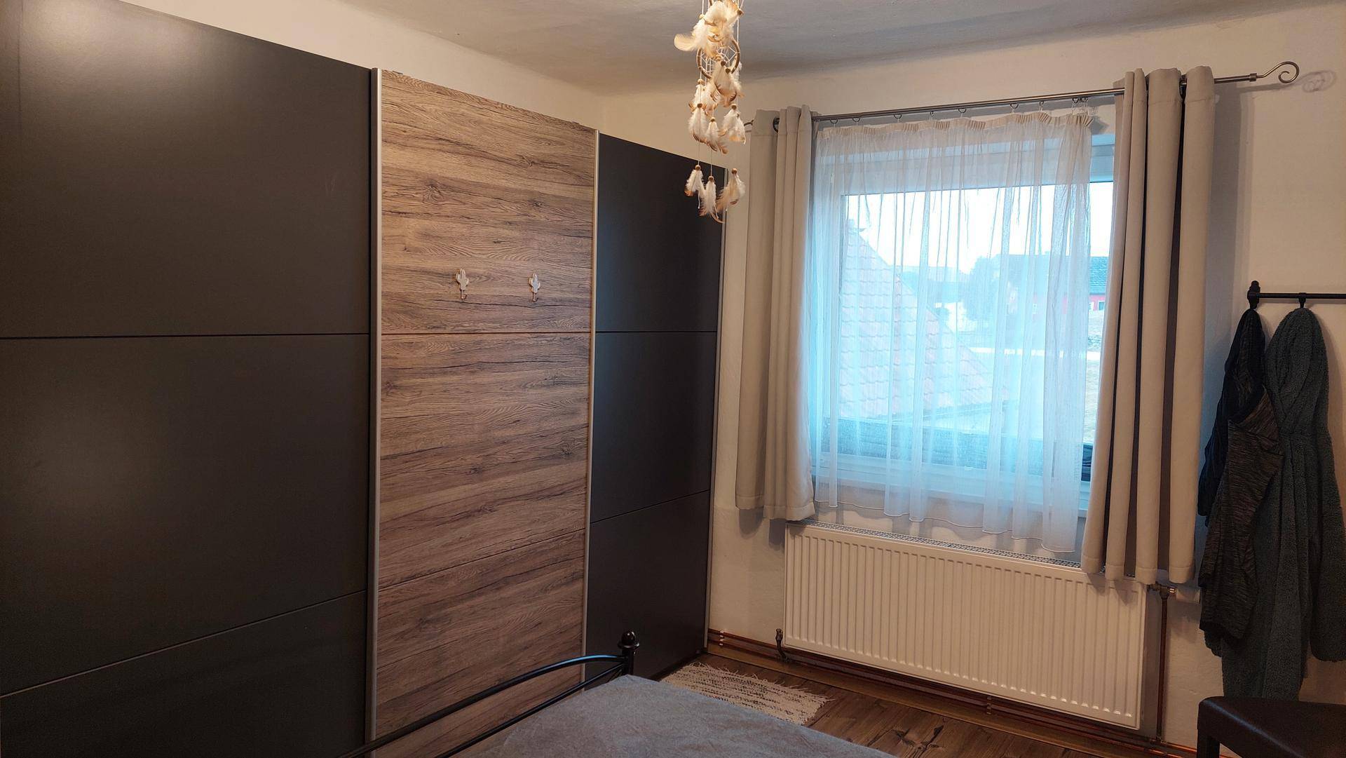 Schlafzimmer mit großem Kleiderschrank und Fenster mit Vorhängen.