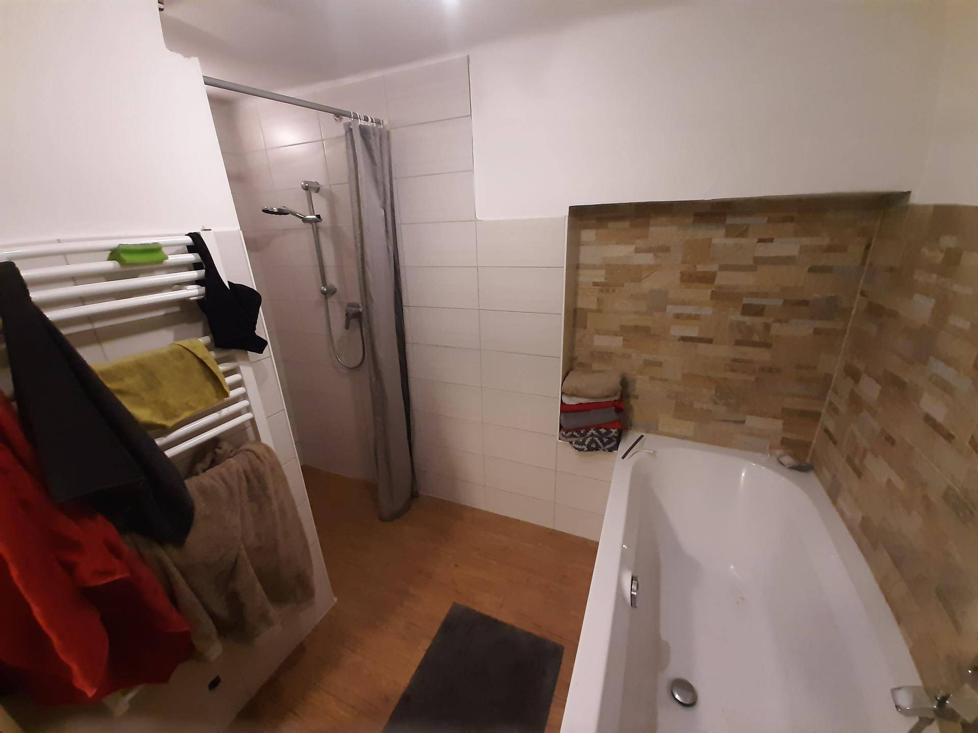 Funktionales Badezimmer mit Badewanne, Duschbereich und beheiztem Handtuchhalter, ergänzt durch eine dekorative Wand.