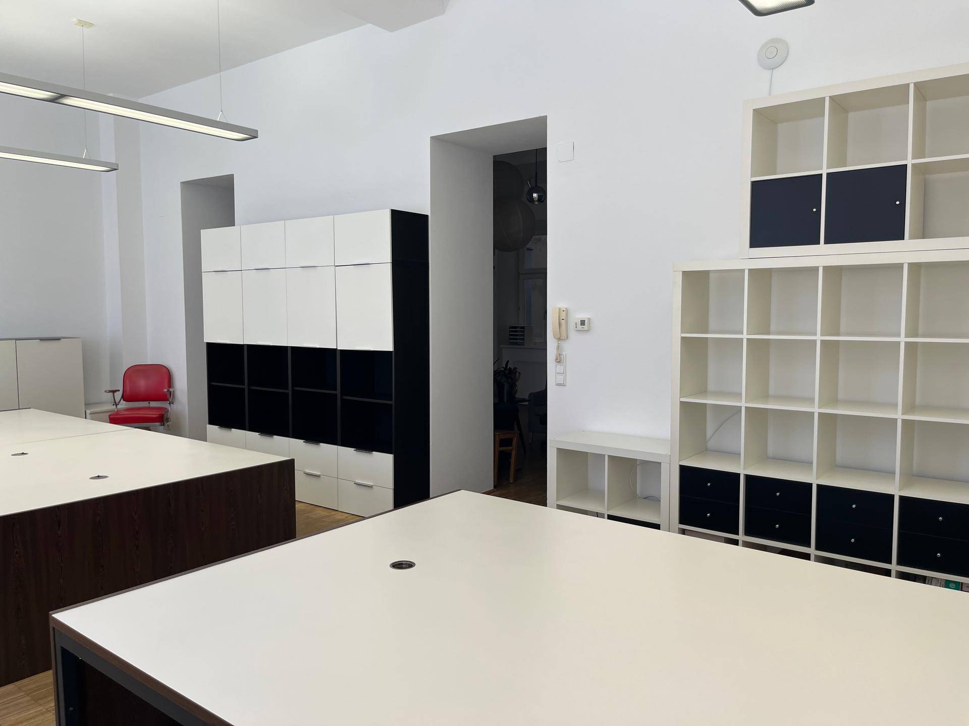 Bürofläche mit offenen Regalen, Schränken und einem Durchgang zu einem weiteren Raum.