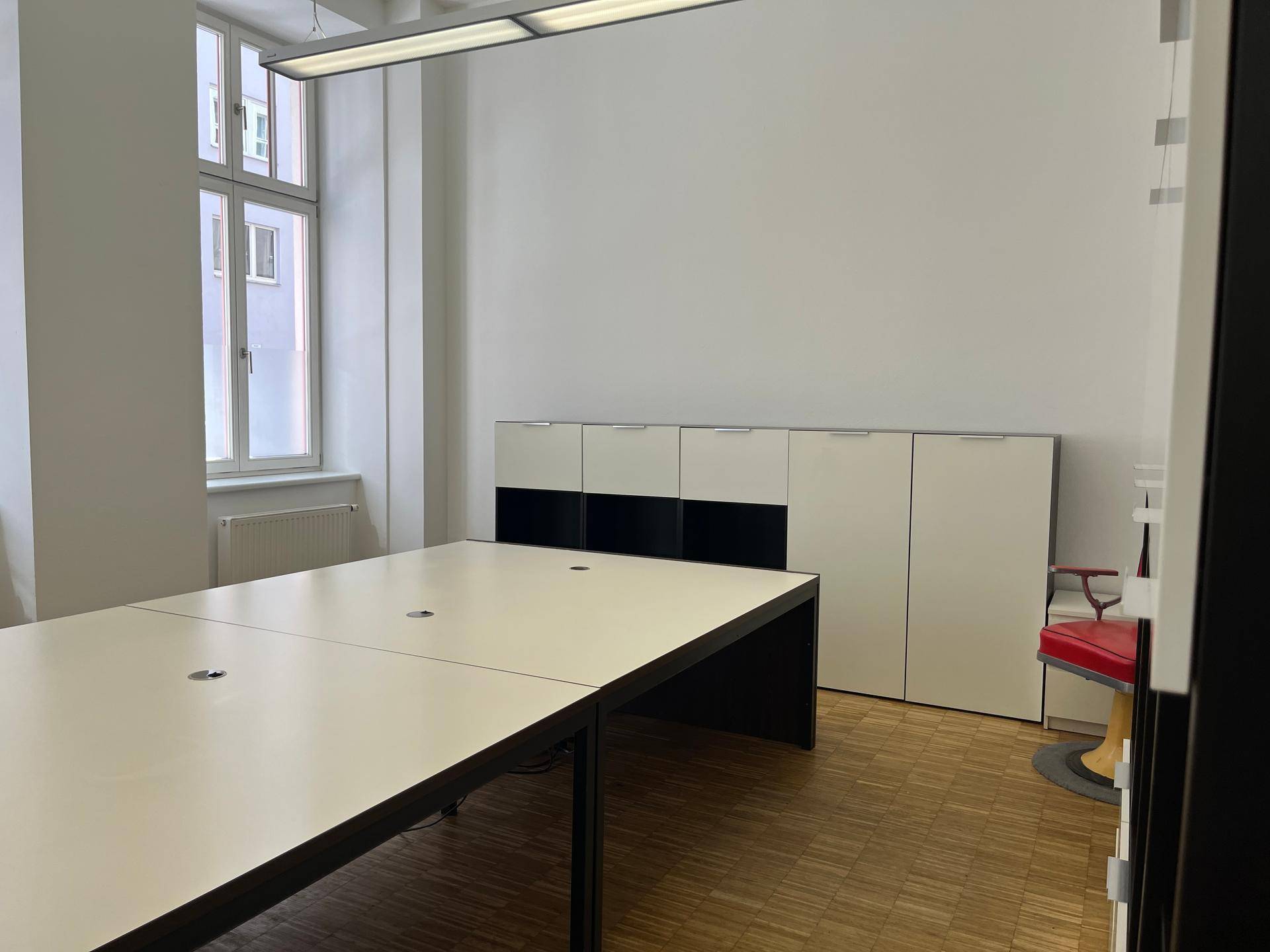 Arbeitsbereich im Büro mit langem Schreibtisch, weißen Schränken und Fensterblick.