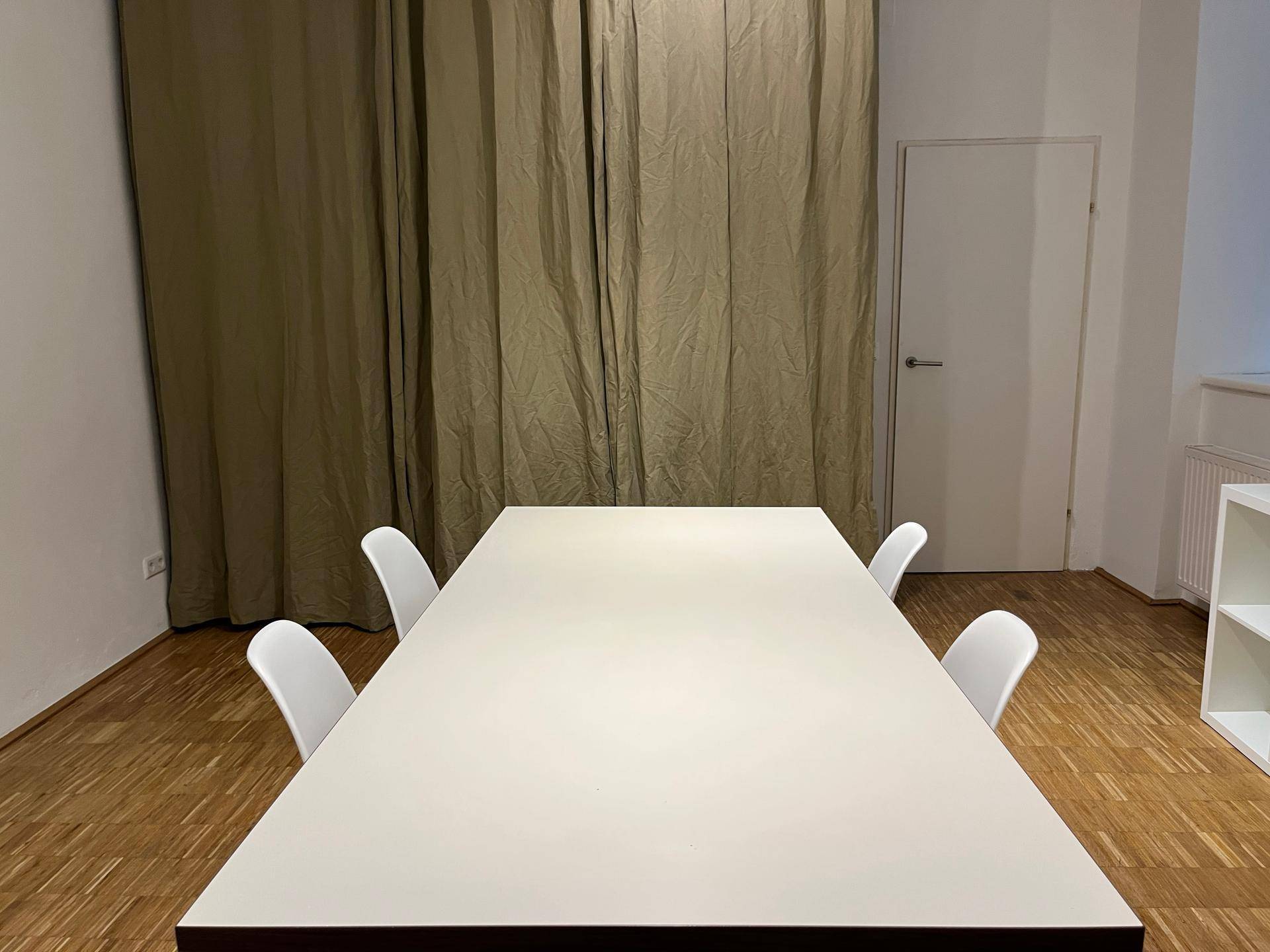 Essbereich mit modernem Tisch und Stühlen, im Hintergrund ein großer Vorhang.