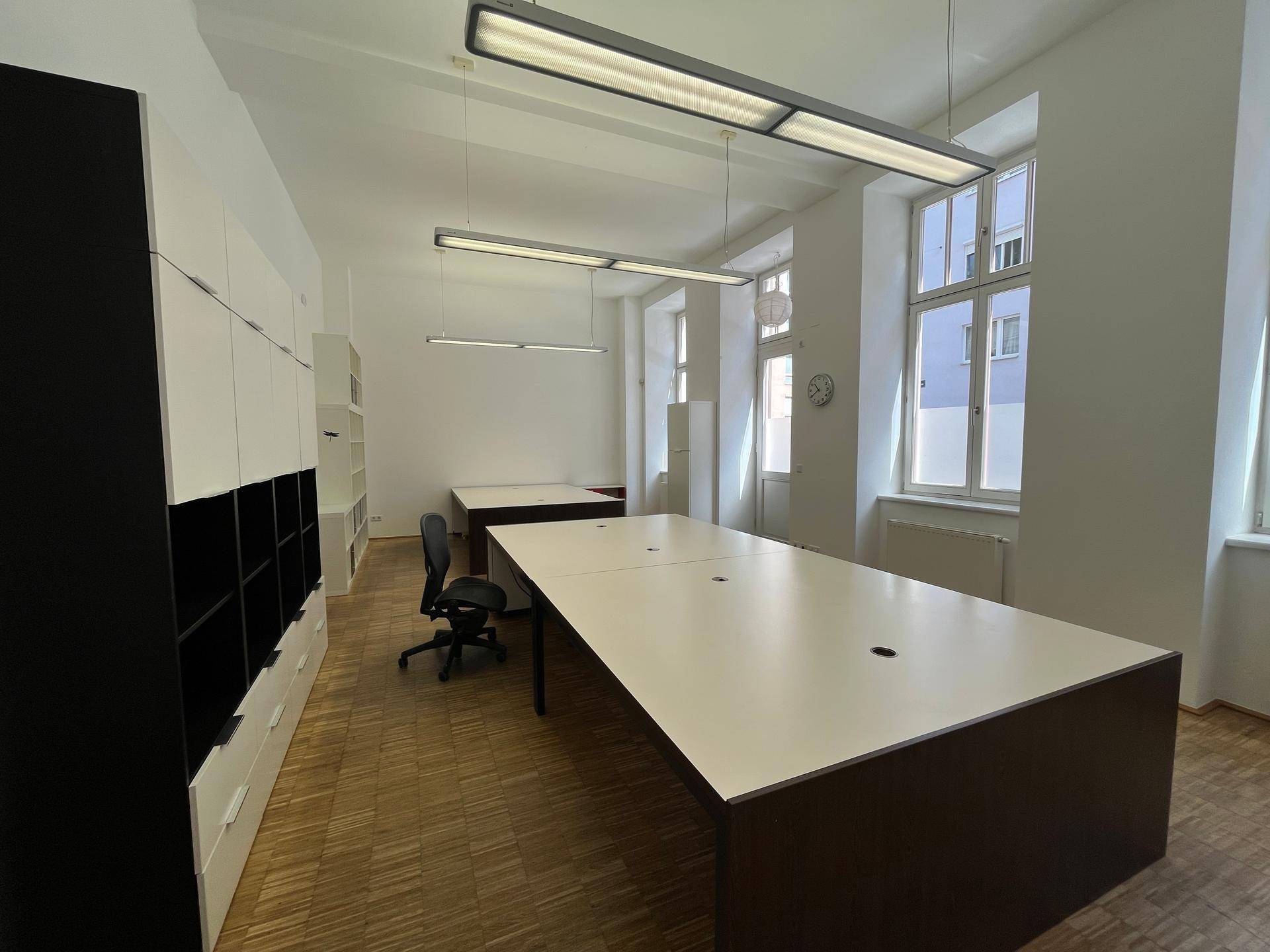 Modernes Büro mit mehreren Arbeitsplätzen, weißen Wänden und Holzparkett.