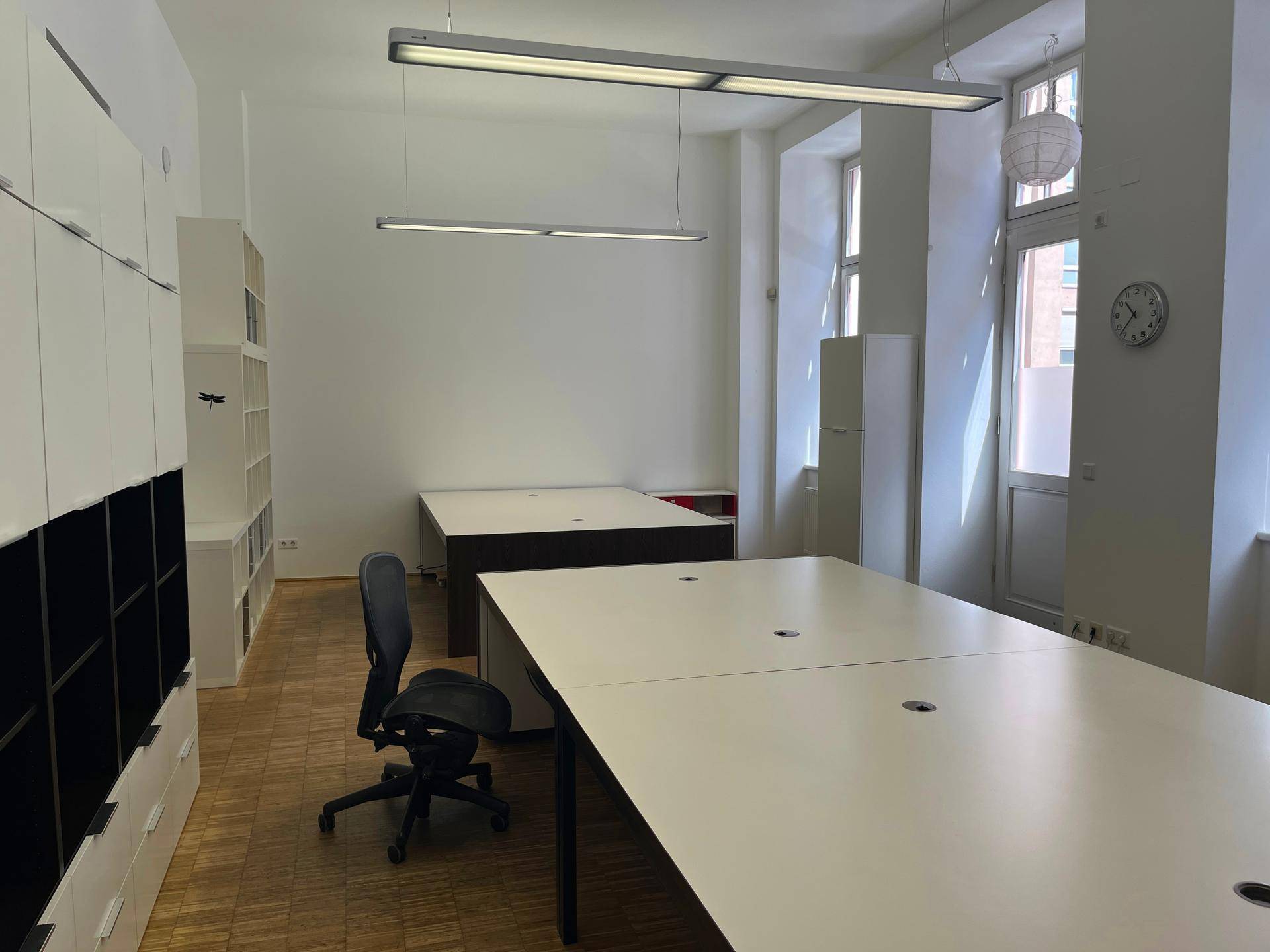 Helles Büro mit funktionalen Schränken, mehreren Schreibtischen und Parkettboden.