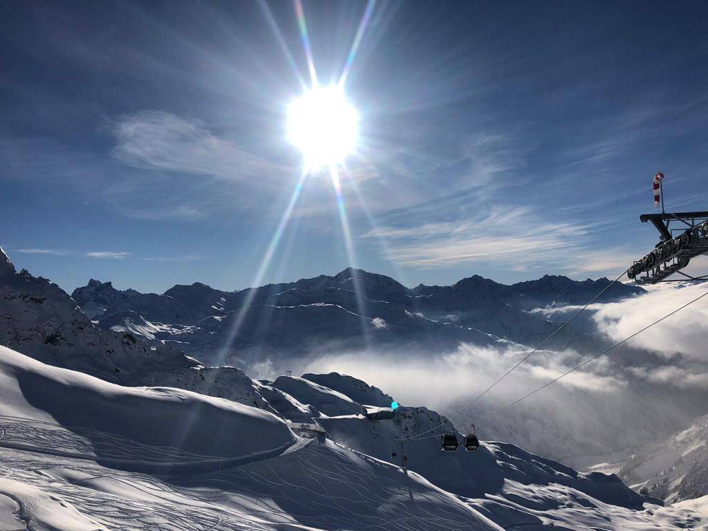 Atemberaubende Winterlandschaft mit verschneiten Bergen, strahlender Sonne und Skilift.